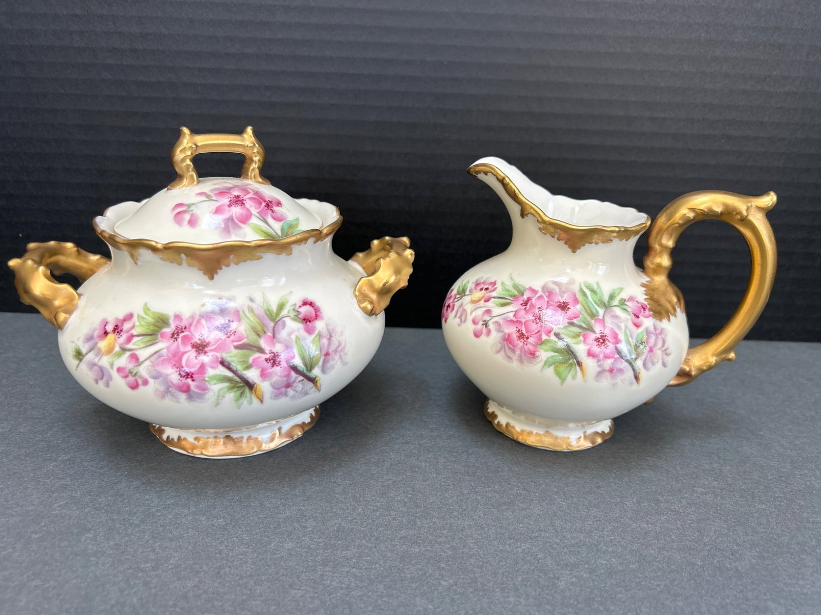 T&V Limoges France Hand-Painted Sugar Bowl and Creamer Set with Gold Detailing: This is a T&V Limoges France hand-painted porcelain sugar bowl and creamer set featuring floral designs with pink flowers and gold accents. Both pieces are marked with the T&V Limoges France logo.