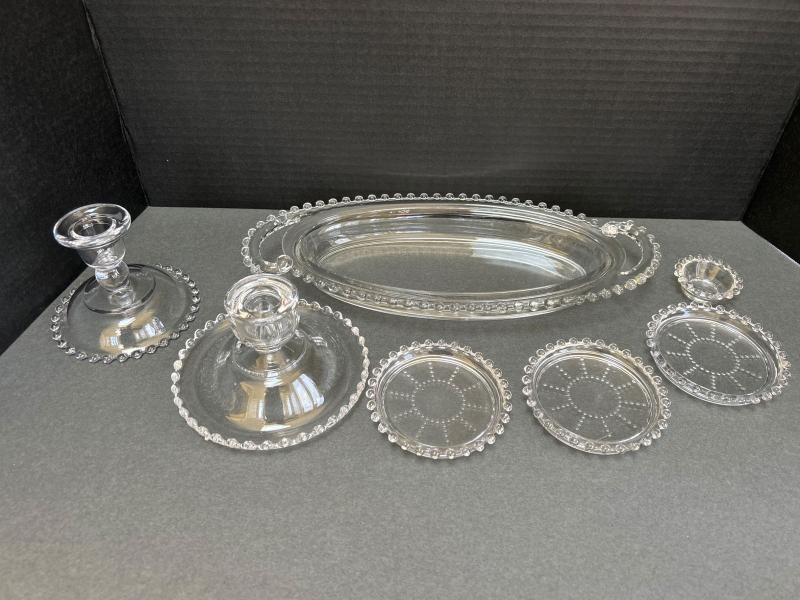 Pressed Glass Serving Set with Beaded Edges, Including Candlesticks and Plates: This lot includes a pressed glass serving set featuring decorative beaded edges. The set consists of two candlesticks, one oval serving tray approximately 11.5 inches long, four round plates with a