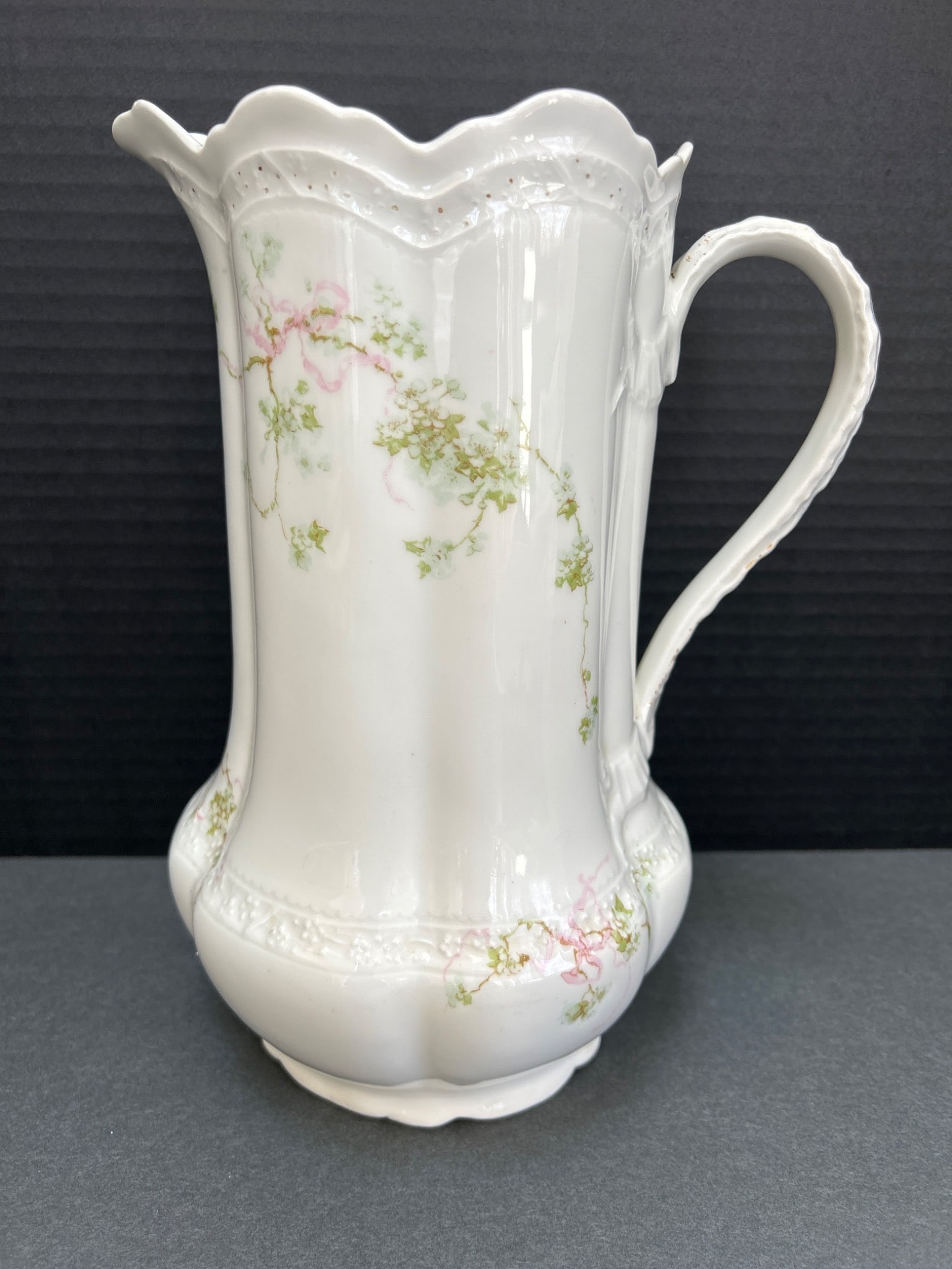 Porcelain Pitcher by Limoges, France with Floral Design: This is a porcelain pitcher crafted in Limoges, France. The pitcher features a delicate floral design with pink and green patterns and a scalloped rim. Measuring approximately 10 inches in height, it