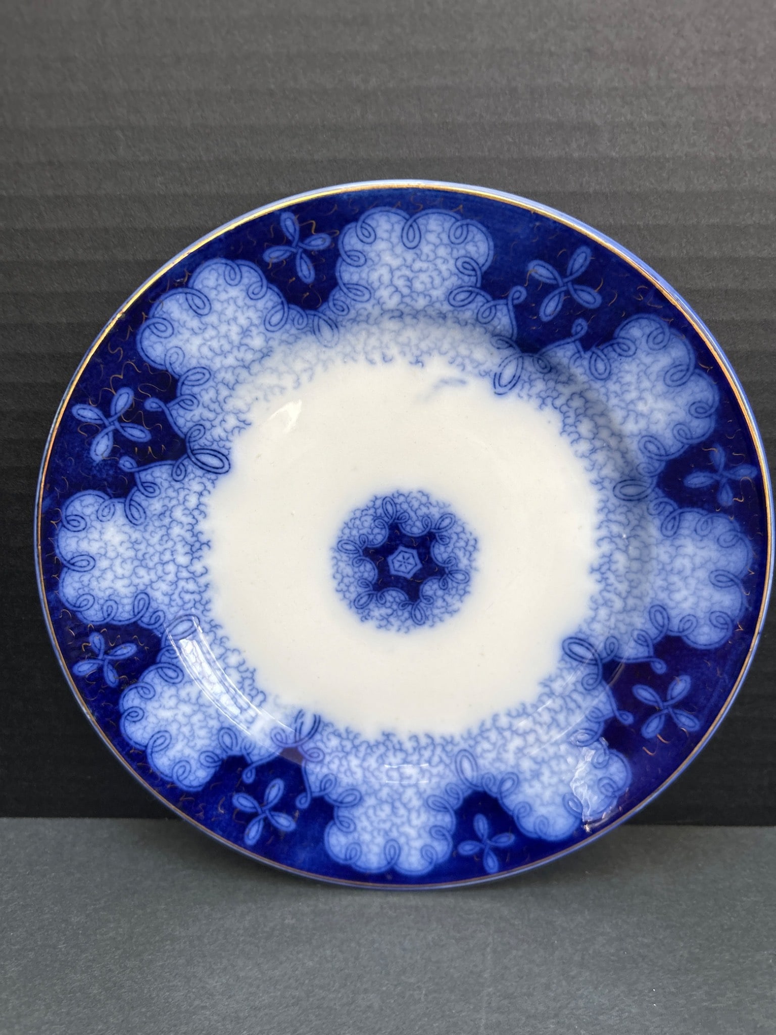 Flow Blue Transferware Plate with Floral Design: This is a ceramic Flow Blue transferware plate featuring a floral design around the edge. It has a cobalt blue decoration and a white center. The backstamp, if present, is not visible in the image, pr