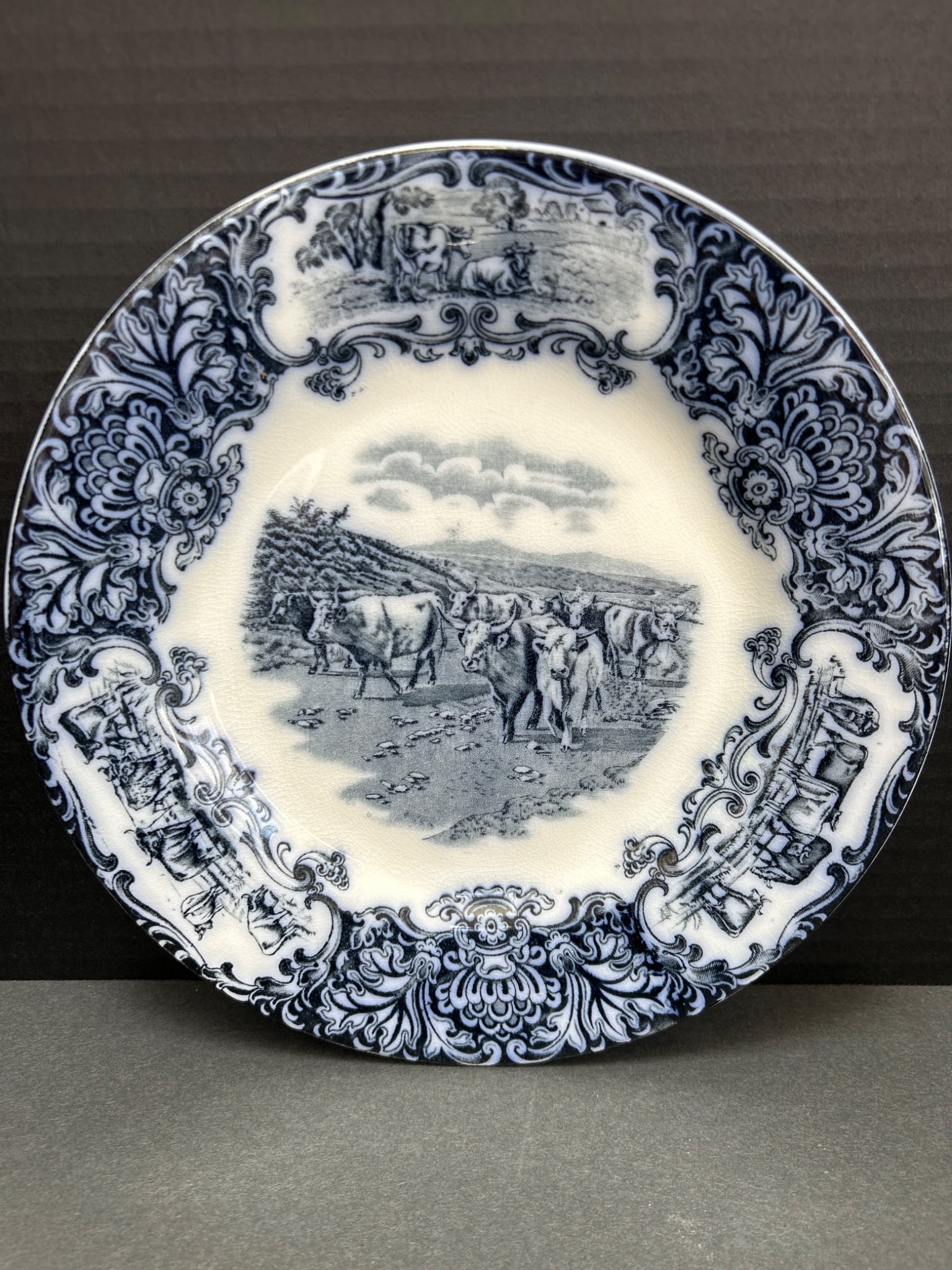 Wedgwood & Co Blue and White Transferware Plate with Scenic Design: This is a blue and white transferware ceramic plate manufactured by Wedgwood & Co, England. It features a pastoral scene with cows in the center surrounded by floral and ornamental patterns. The