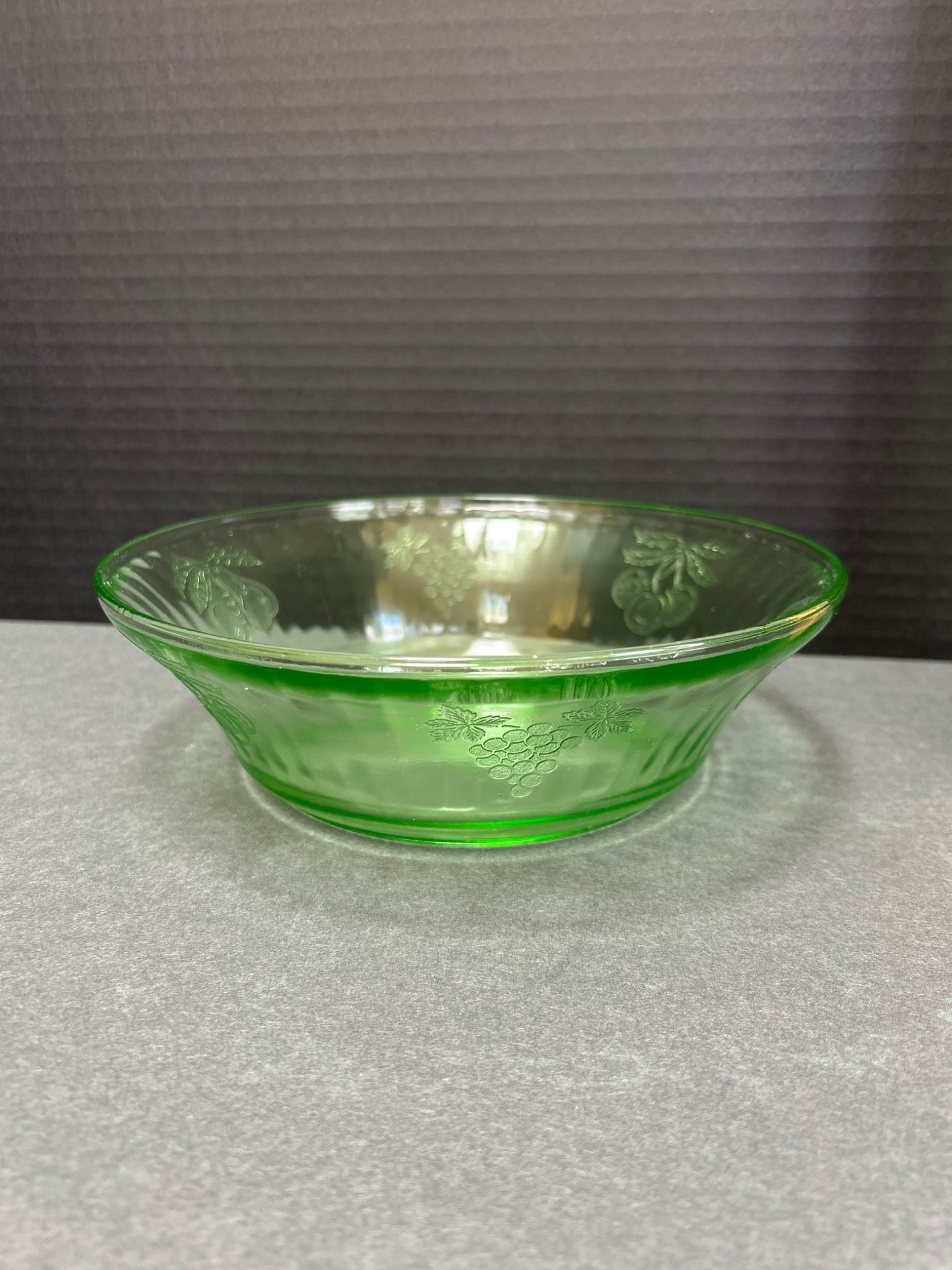 Green Depression Glass Bowl With Embossed Cherry and Grape Patterns: This is a green depression glass bowl featuring embossed cherry and grape patterns on the exterior and base. It measures approximately 6.5 inches in diameter and about 2 inches in height. The bowl