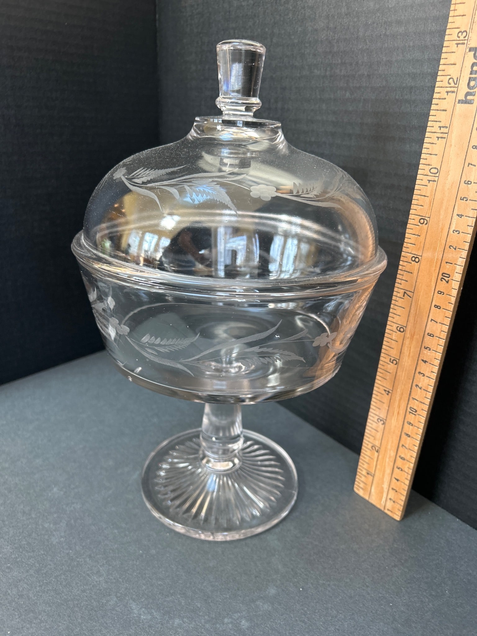 Clear Lidded Glass Compote with Etched Floral Design and Pedestal Base: This is a clear glass compote featuring a lid and an etched floral design. The compote is mounted on a pedestal base with radial patterns on the foot. The lid includes a knob handle for easy lifting.