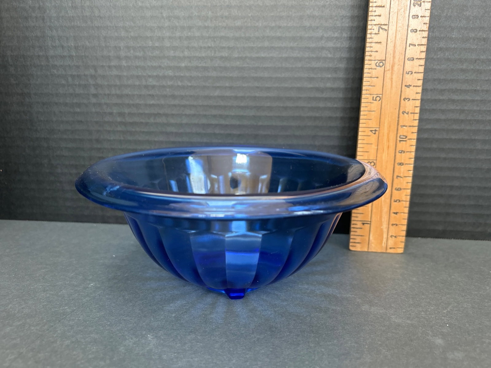 Blue Fluted Glass Bowl With Rounded Base Design: A blue fluted glass bowl featuring a rounded base with a raised pedestal-like structure. Approximate measurements: 4 inches in diameter and 2 inches in height. The bowl exhibits a symmetrical ribbed