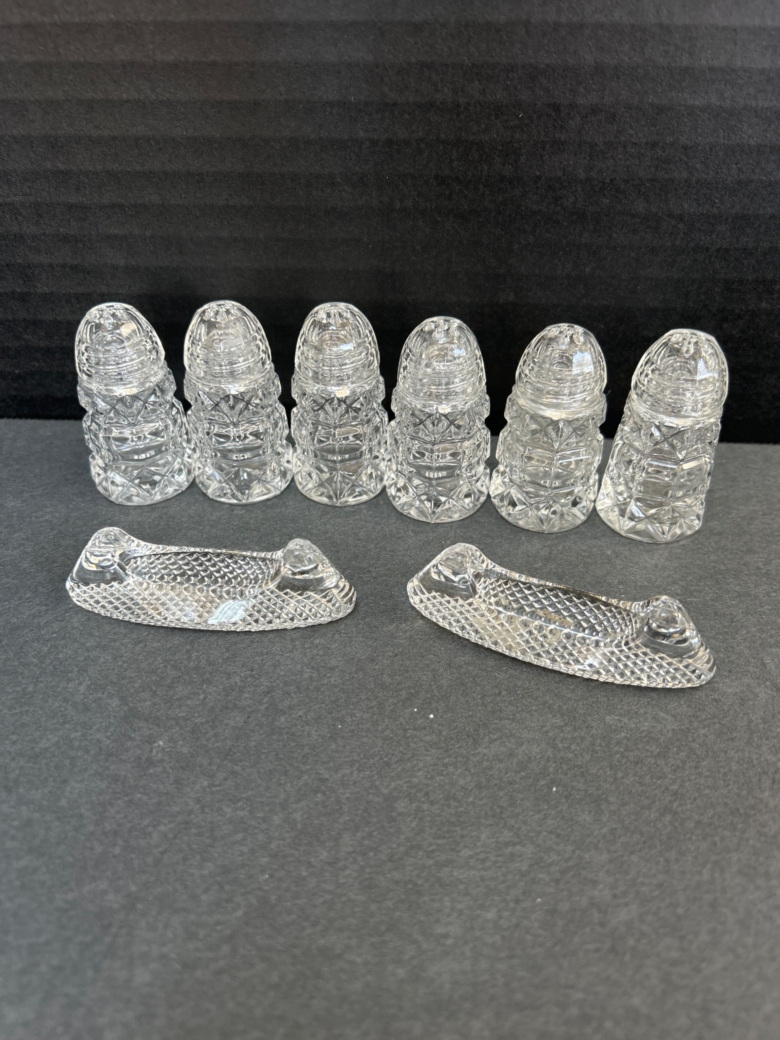 Cut Glass Salt Shakers and Knife Rests, 7 Pieces: Five cut glass salt shakers and two knife rests. Shakers feature a faceted design with a domed top, likely for dispensing salt or similar condiments, while the knife rests have textured detailing.