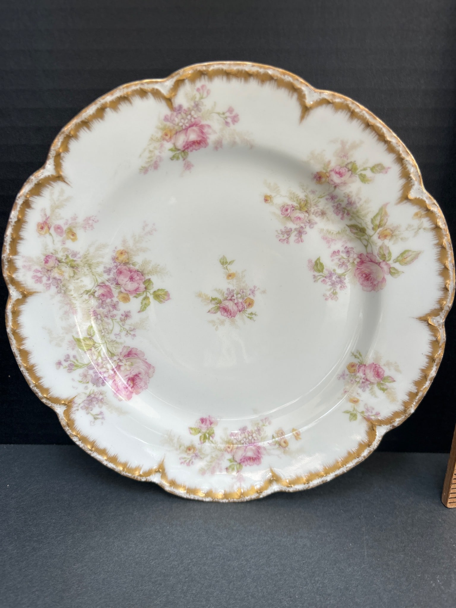 Haviland France Plate with Pink Floral Design and Gold Trim: This plate was manufactured by Haviland & Co. in Limoges, France, as indicated by the backstamp. It features a pink floral design with gold trim along the scalloped edges. The plate measures