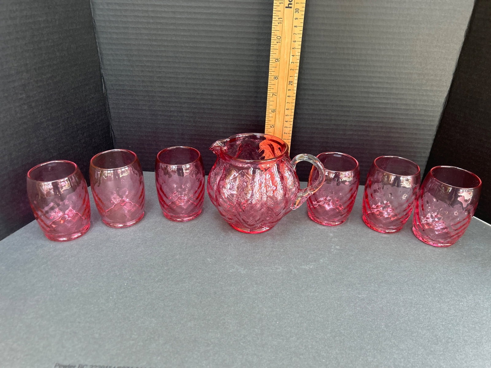 Pink Glass Pitcher and Six Matching Glasses Set with Diamond Pattern: This lot includes a pink glass pitcher and six matching small glasses, each featuring a diamond pattern design. The pitcher has a spouted design with a glass handle, and the glasses are cylindrical