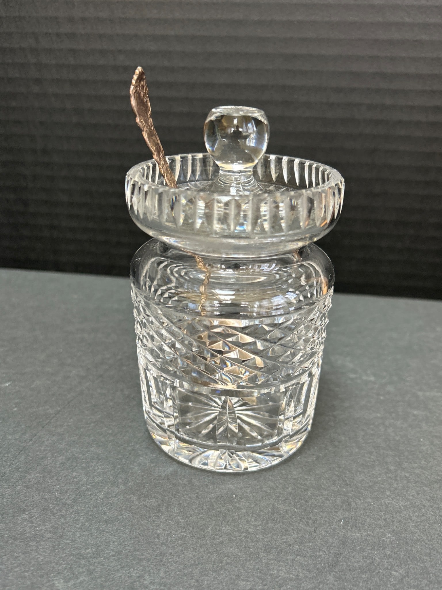 Cut Glass Condiment Jar With Sterling Silver Spoon: This lot includes a cut glass condiment jar featuring a detailed diamond-cut design. The jar measures approximately 4 inches in height and includes a fitted lid with a knob handle. Accompanying the