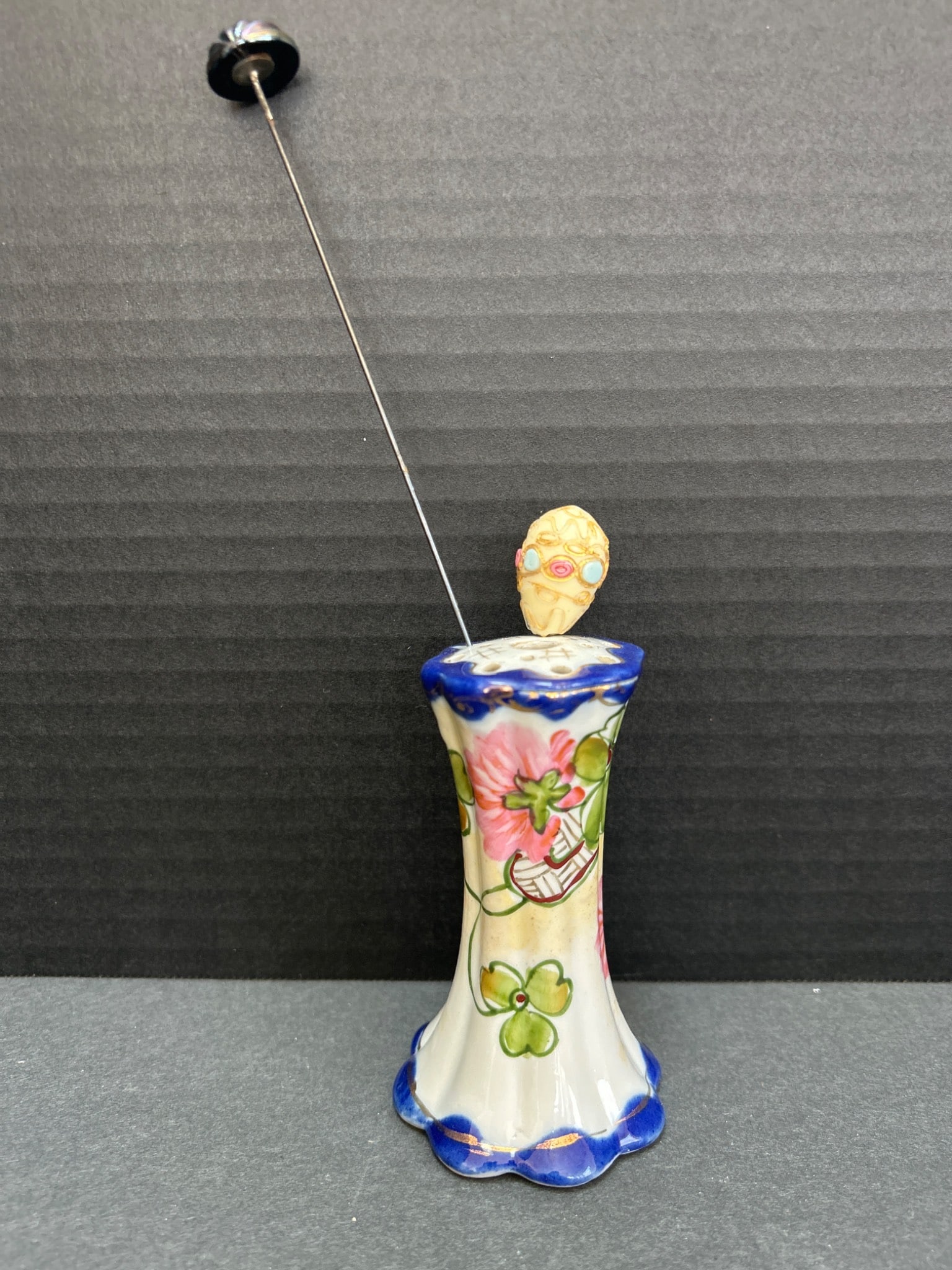 Hand-Painted Ceramic Hatpin Holder with Floral Design and Scalloped Base: Hand-painted ceramic hatpin holder measuring approximately 4.5 inches tall. Features a decorative floral design with a scalloped base, blue border accents, and multicolor embellishments. Includes a