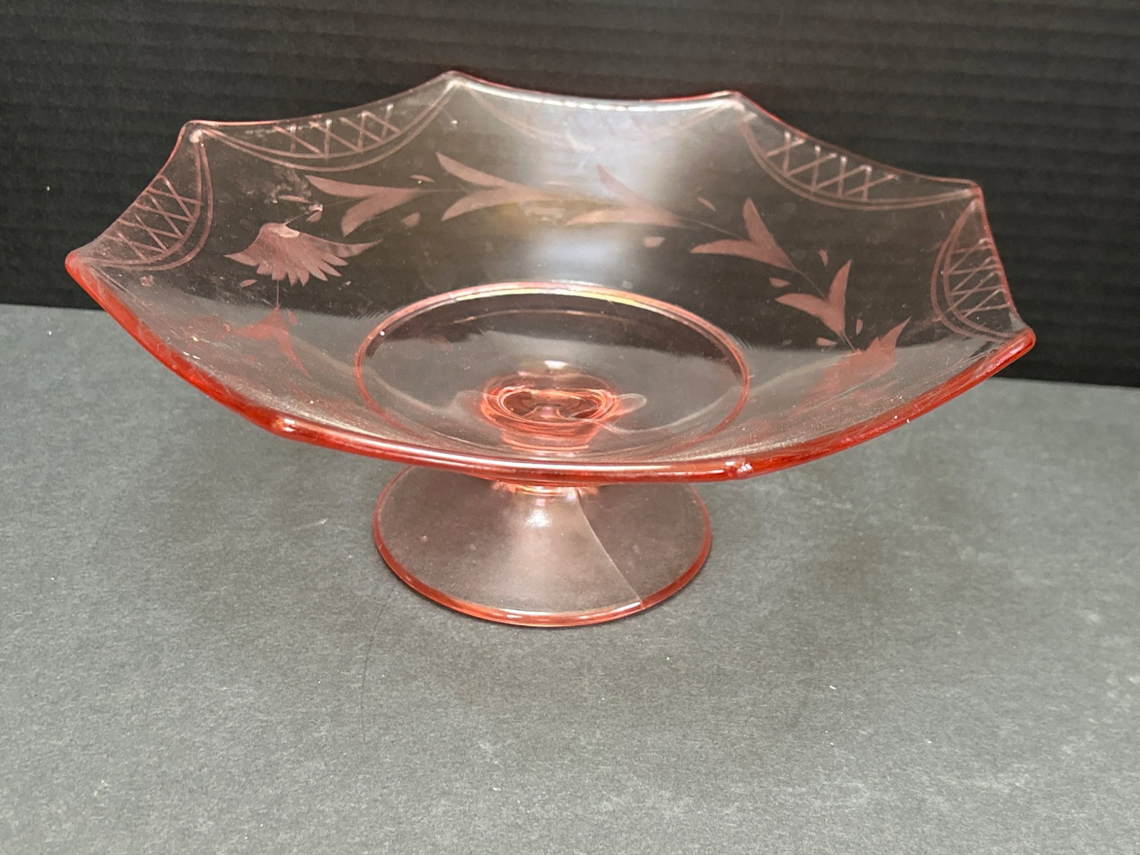 Pink Glass Pedestal Compote With Engraved Bird Motif and Geometric Design: This is a pink glass pedestal compote featuring an engraved bird and geometric motif. The compote has an octagonal dish and measures approximately 8 inches in diameter as shown in the image with the