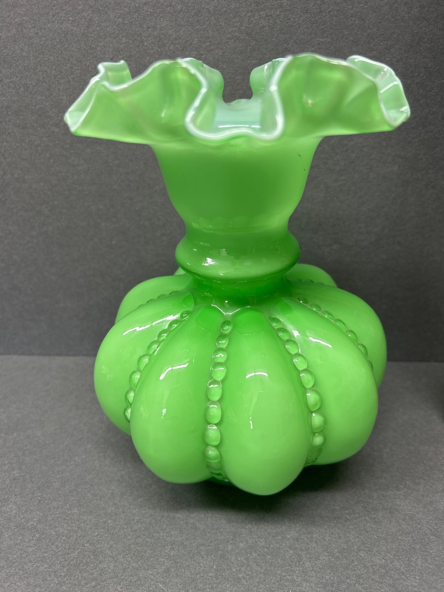 Green Ruffled Glass Vase With Beaded Design: This is a green glass vase featuring a ruffled top and a beaded pattern on its bulbous base. The vase measures approximately 5 inches in height as depicted next to a ruler. The craftsmanship appears