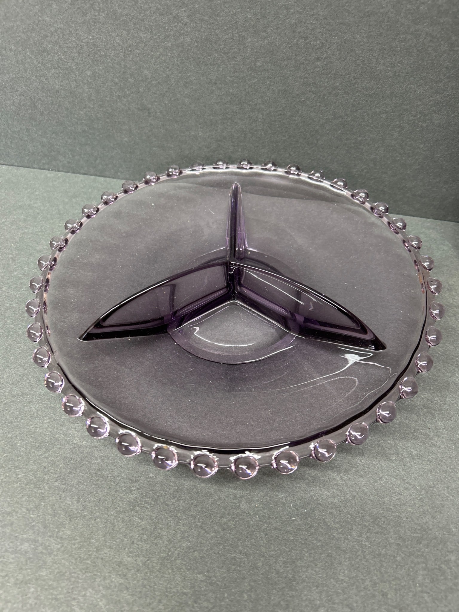 Purple Glass Divided Serving Dish With Beaded Rim: Purple glass divided serving dish featuring a 3-section design and a decorative beaded rim. Measures approximately 9.5 inches in diameter. Exact year of manufacture and maker unknown. Overall
