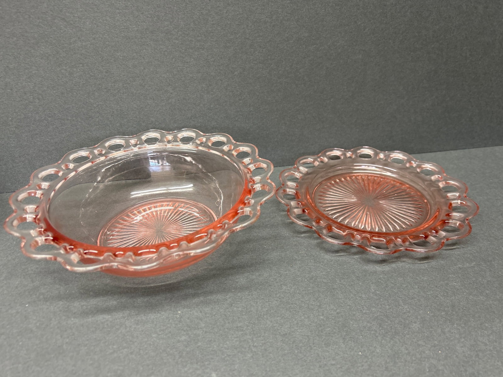 Two Pink Glass Bowls with Laced Rim and Starburst Pattern: This is a set of two pink glass bowls featuring a laced rim design and a starburst pattern on the base. The larger bowl measures approximately 8 inches in diameter, while the smaller bowl measures