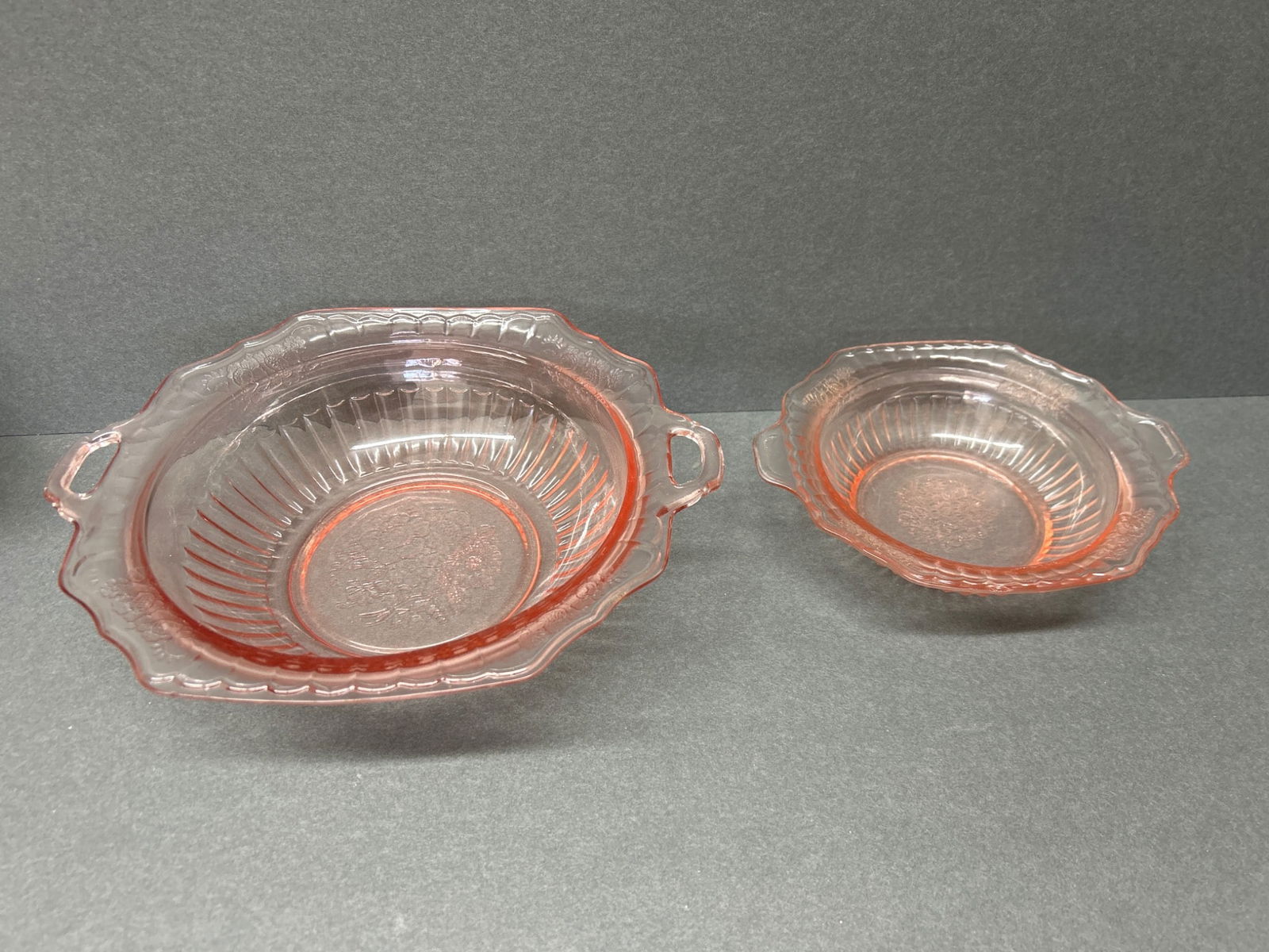 Two Pink Depression Glass Bowls with Floral Pattern and Handles: This lot includes two pink glass bowls featuring a floral motif at the center and handles on either side. The bowls appear to belong to the Depression glass era but lack explicit model or maker