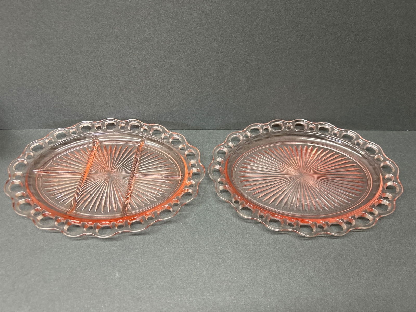 Pink Depression Glass Oval Plates with Open Lace Edge, Set of 2: This set includes two pink Depression glass oval plates with an open lace edge design. One plate features a divided section, while the other remains undivided. Both exhibit a starburst pattern in the