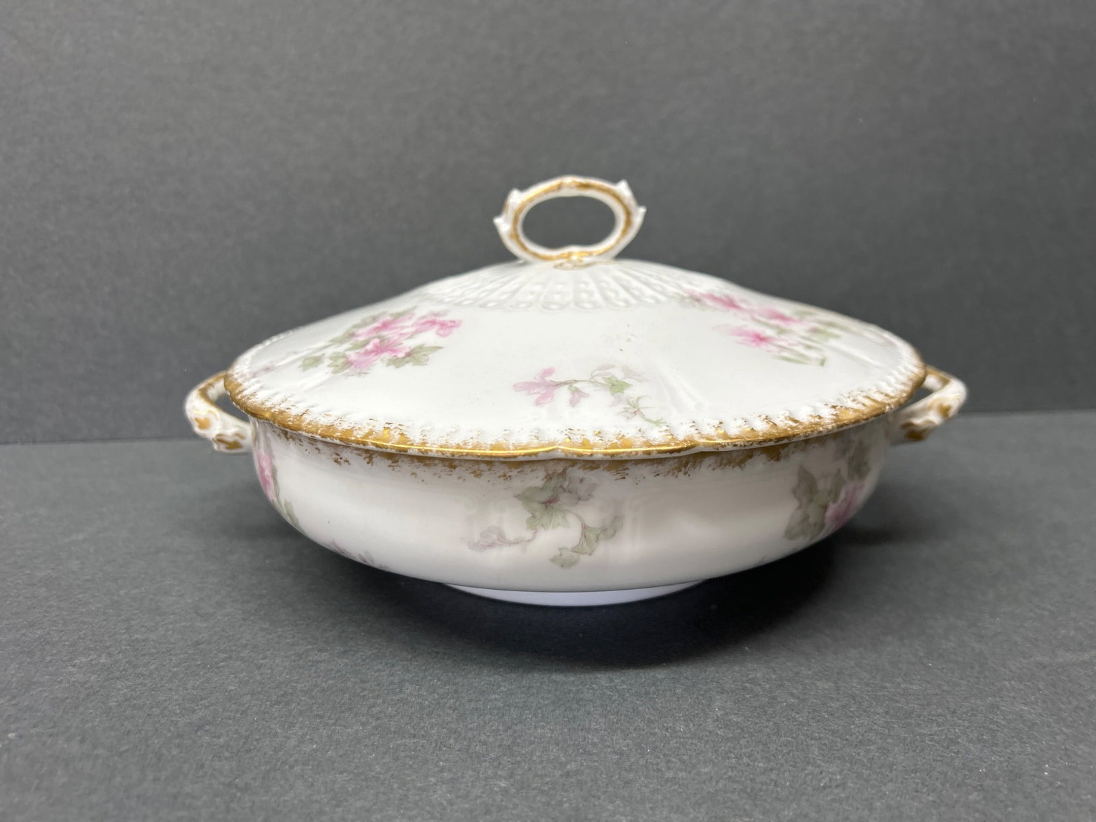 Limoges France GDA Porcelain Covered Dish with Floral Design and Gold Accents: This porcelain covered dish is marked 'GDA France' and 'GDA Limoges'. It features a floral design in pink and green colors with gold accents on the handle and edges. The lid has a decorative central