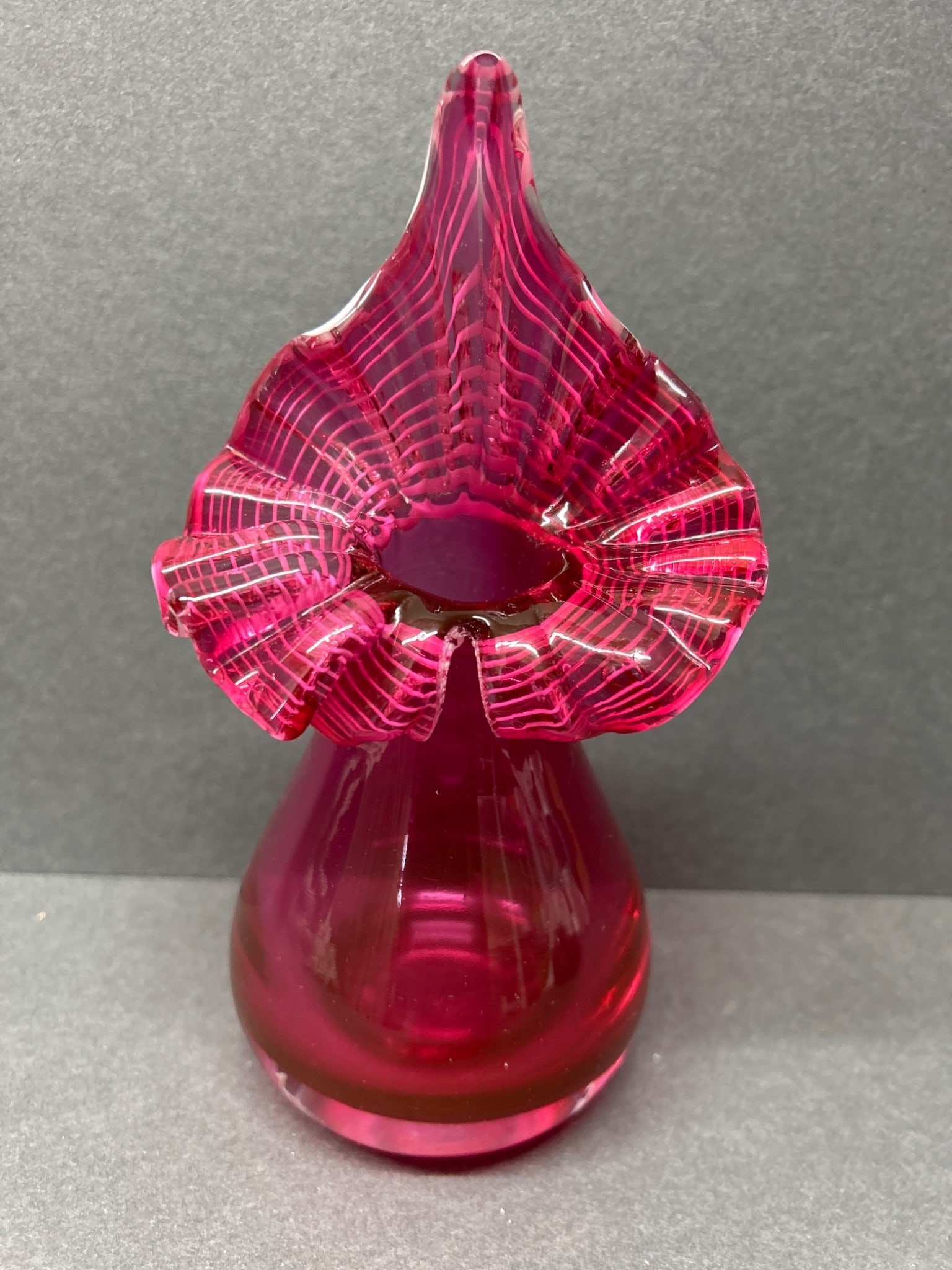 Handblown Art Glass Vase With Flaring Ruffled Top in Deep Pink: This is a handblown art glass vase in a deep pink hue. The vase features a ruffled top with white-striped accents, and a smooth rounded base. The approximate height is 6 inches based on the accompanyi