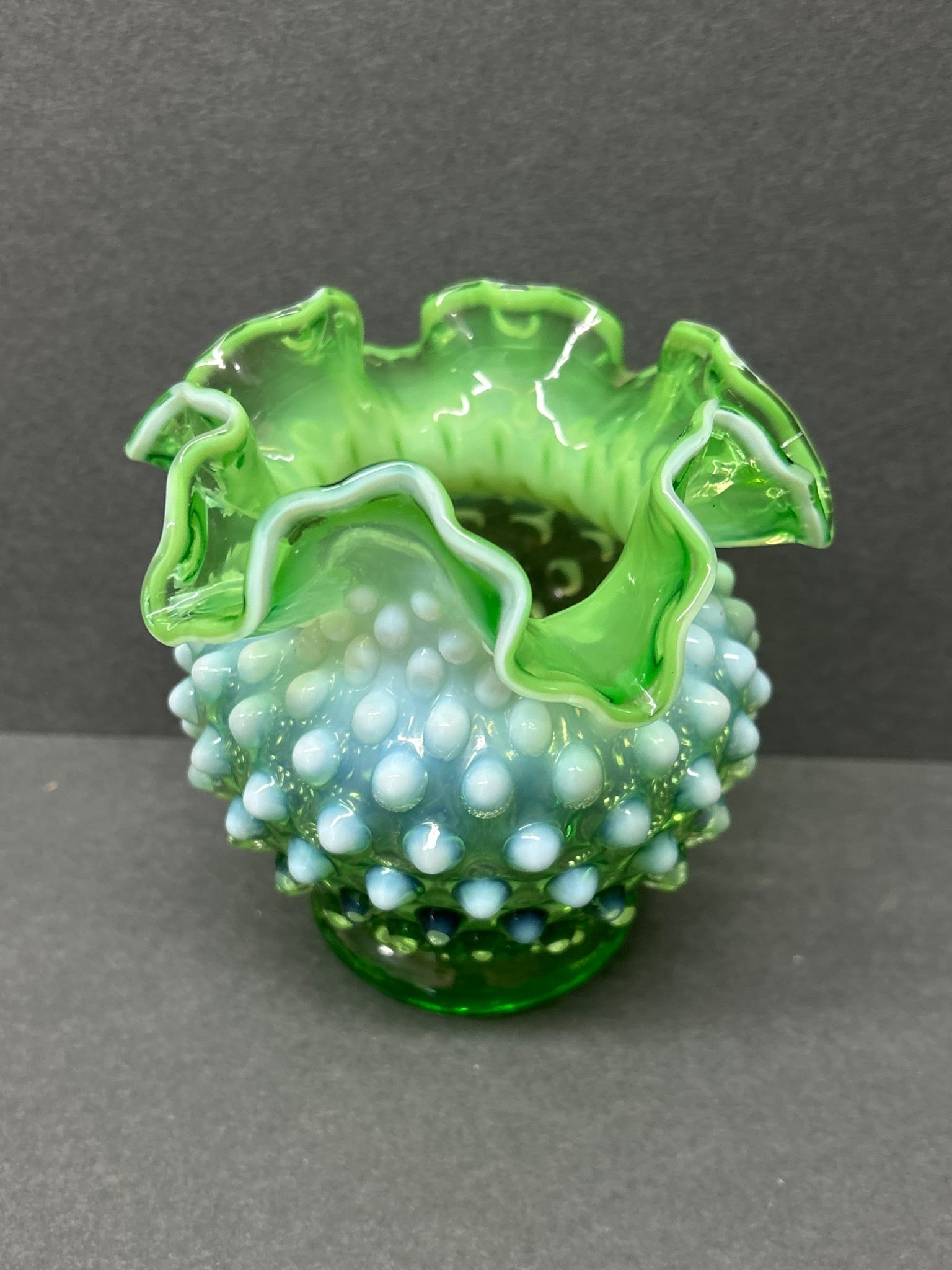 Green Opalescent Hobnail Glass Vase with Ruffled Rim: A small green opalescent glass vase featuring a hobnail texture and ruffled rim, as shown in the images. Measures approximately 4 inches in height. The piece showcases a vibrant green base transitioni