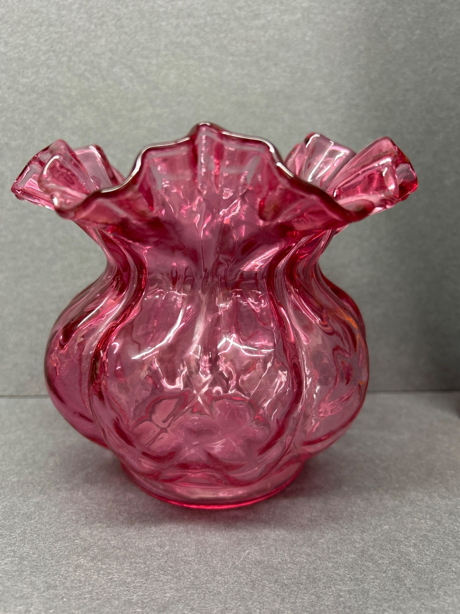 Glass Vase With Pink Ruffled Rim and Embossed Design: This is a small decorative glass vase featuring a pink transparent body with an embossed floral ornamentation and a ruffled rim. Measuring approximately 4 inches in height, the vase showcases a polish