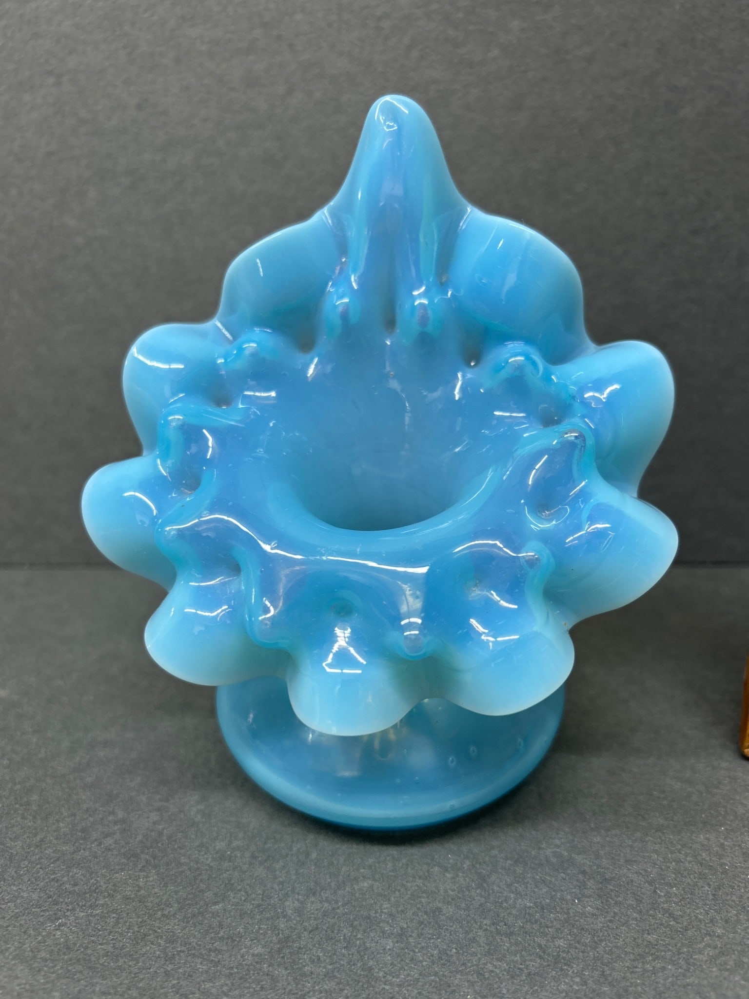 Blue Glass Vase With Ruffled Edges - Approximately 5 Inches Tall: Blue glass vase featuring a ruffled edge design and a smooth base. Approximate height is 5 inches as indicated by a ruler in the photos. The upper portion of the vase has a central opening, while the