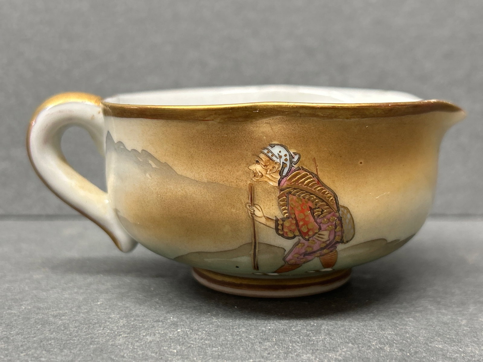Porcelain Cup With Hand-Painted Landscape And Figure Decor, Marked Base: A porcelain cup featuring a hand-painted landscape and figure theme. The design includes detailed depictions of people and structures. The base displays a red mark, commonly representing the maker or