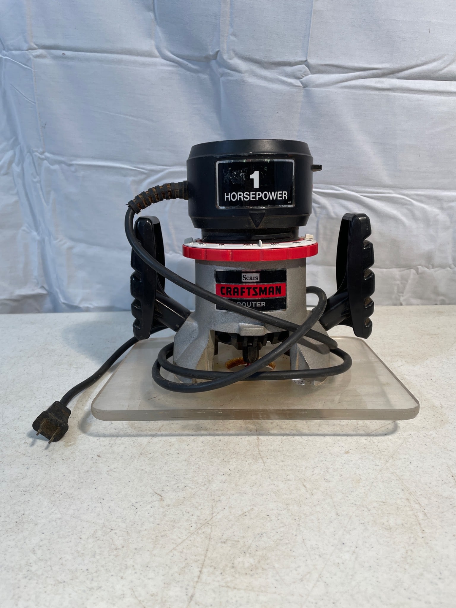 Craftsman 1 Horsepower Double Insulated Router Model 315.174921: This is a Craftsman 1 horsepower double insulated router, model number 315.174921. The unit includes two ergonomic handles and is mounted on a clear plastic base plate. Electrical plug and cord are in