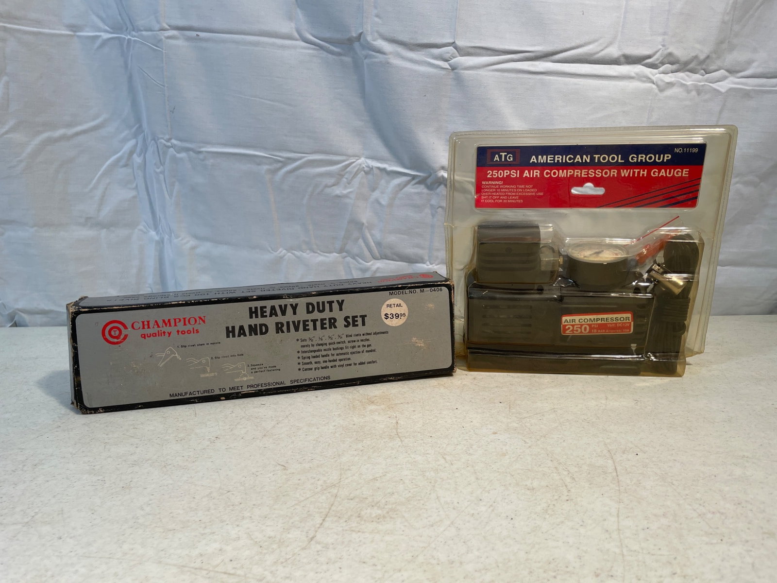 Champion Heavy Duty Hand Riveter Set and 25 PSI Air Compressor with Gauge: This lot includes a Champion heavy-duty hand riveter set with original packaging, featuring various rivet sizes and a blue riveter tool. Also included is an American Tool Group 25 PSI air compressor w