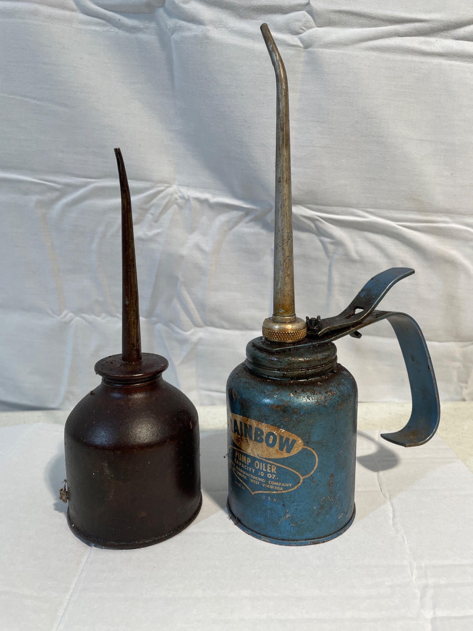 Oil Cans: Rainbow Pump Oiler and Unmarked Oiler: The lot includes two oil cans: a Rainbow Pump Oiler with a capacity of 10 oz, manufactured by EAGLE Manufacturing Co., Wellsburg, West Virginia, USA, and an unmarked dark oil can with a long spout. Th
