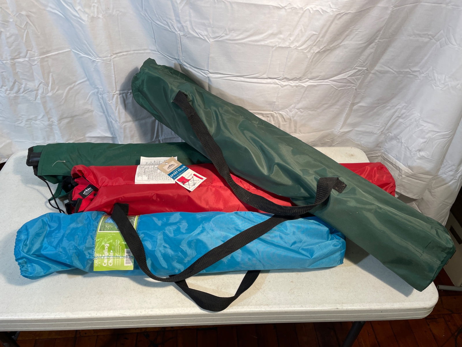 Four Folding Camping Chairs with Carry Bags: Four folding camping chairs, each packed in its original carry bag. Includes chairs in different colors (blue, red, and two green). One is labeled 'Northwest Territory Sport Chair,' and another
