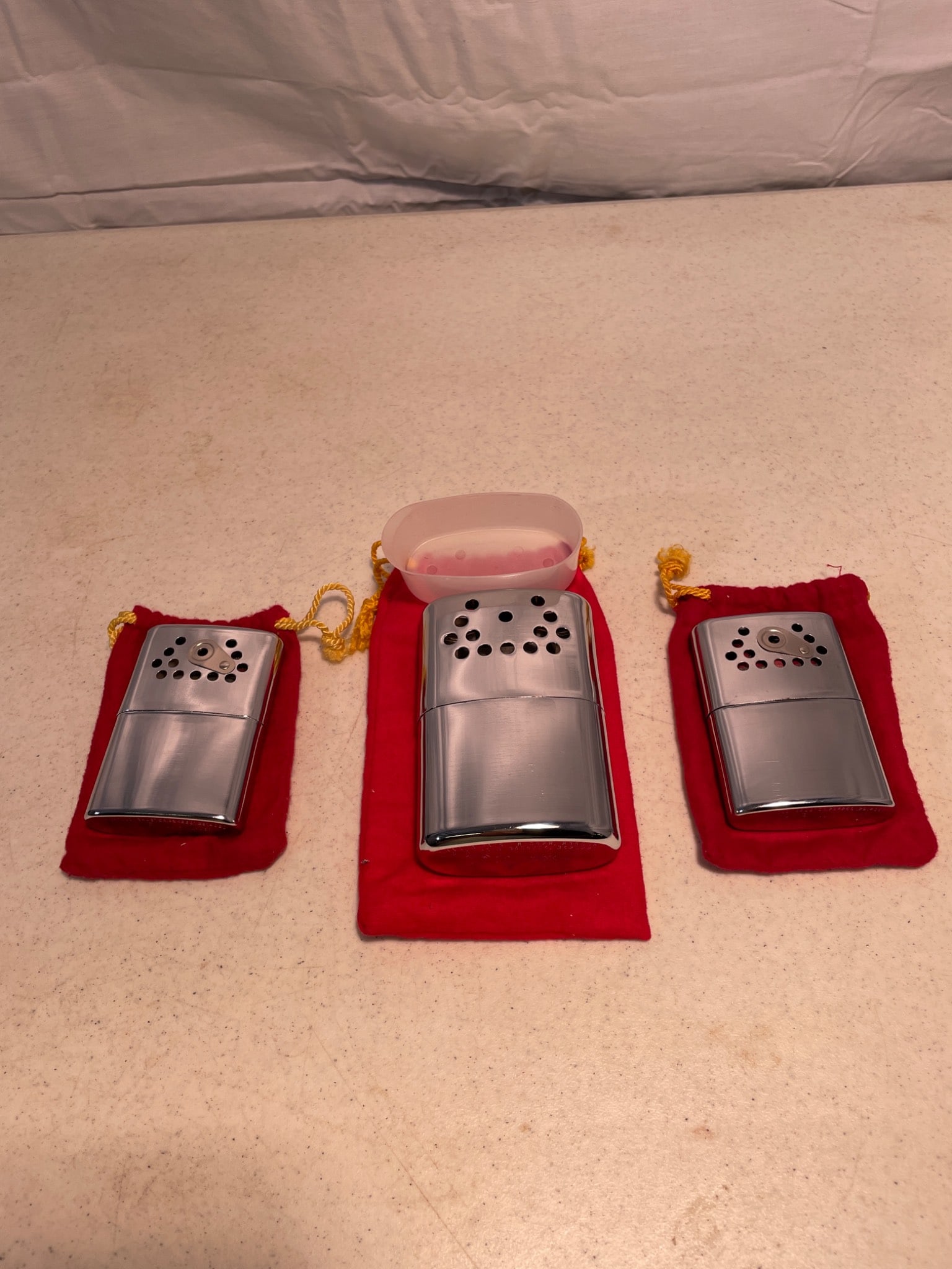 3 Jon-E Hand Warmers with Red Pouches, Made in USA: This lot consists of three Jon-E hand warmers made in the USA. The bottom of each unit is marked with patent information, including 'Patented 1976 1965 1950' and 'Hand Warmer, Made in MPLS, Minn.'
