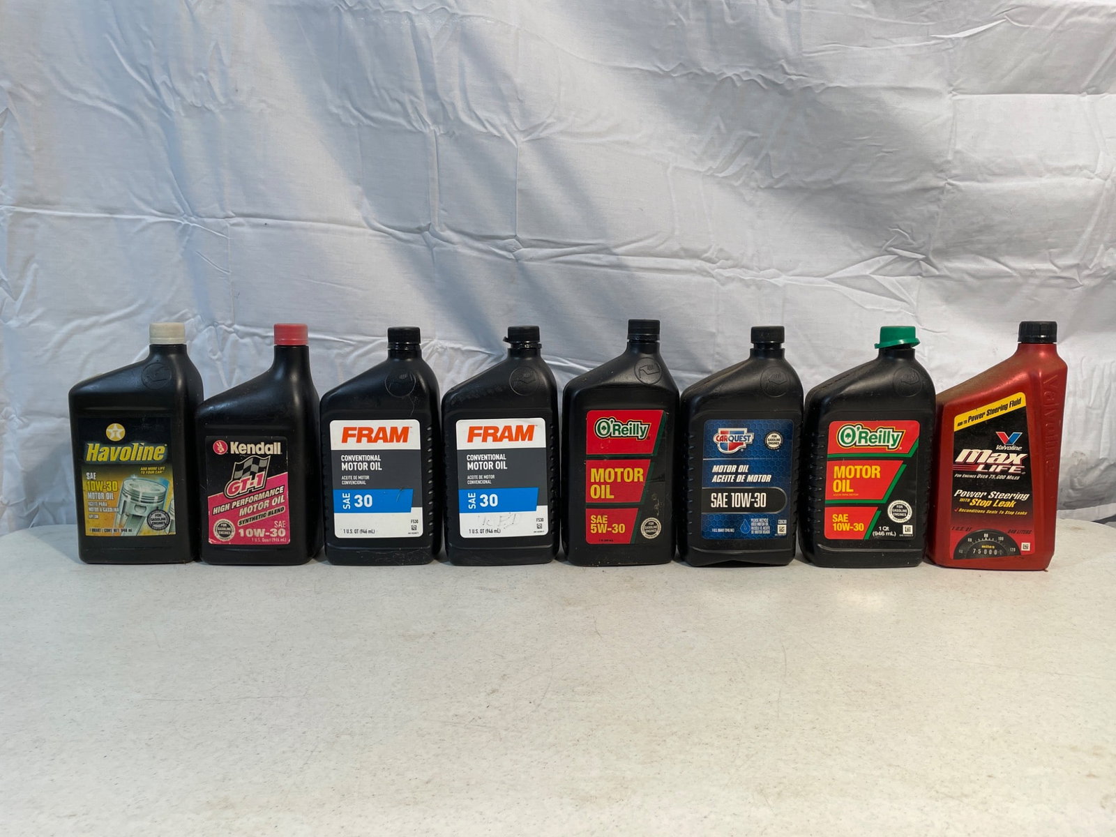 8 Assorted Motor Oils - Various Brands and Grades: This lot includes 8 assorted motor oil containers from various brands. Each container appears unopened, with labels indicating specifications such as viscosity grades and certifications. Brands includ