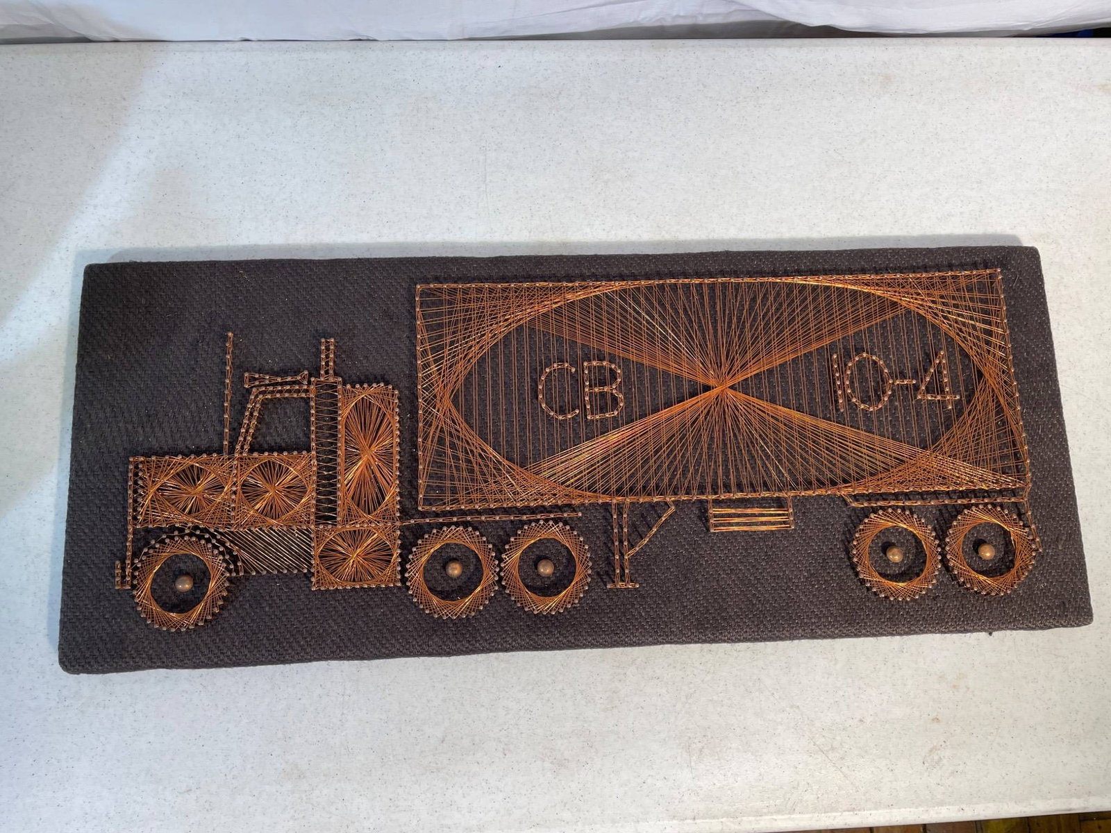 Folk Art String and Nail Truck Design Wall Art: A rectangular piece of folk art depicting a truck design using string and nails on a solid board backing. The piece is crafted with precision, creating a visually intricate composition of the truck