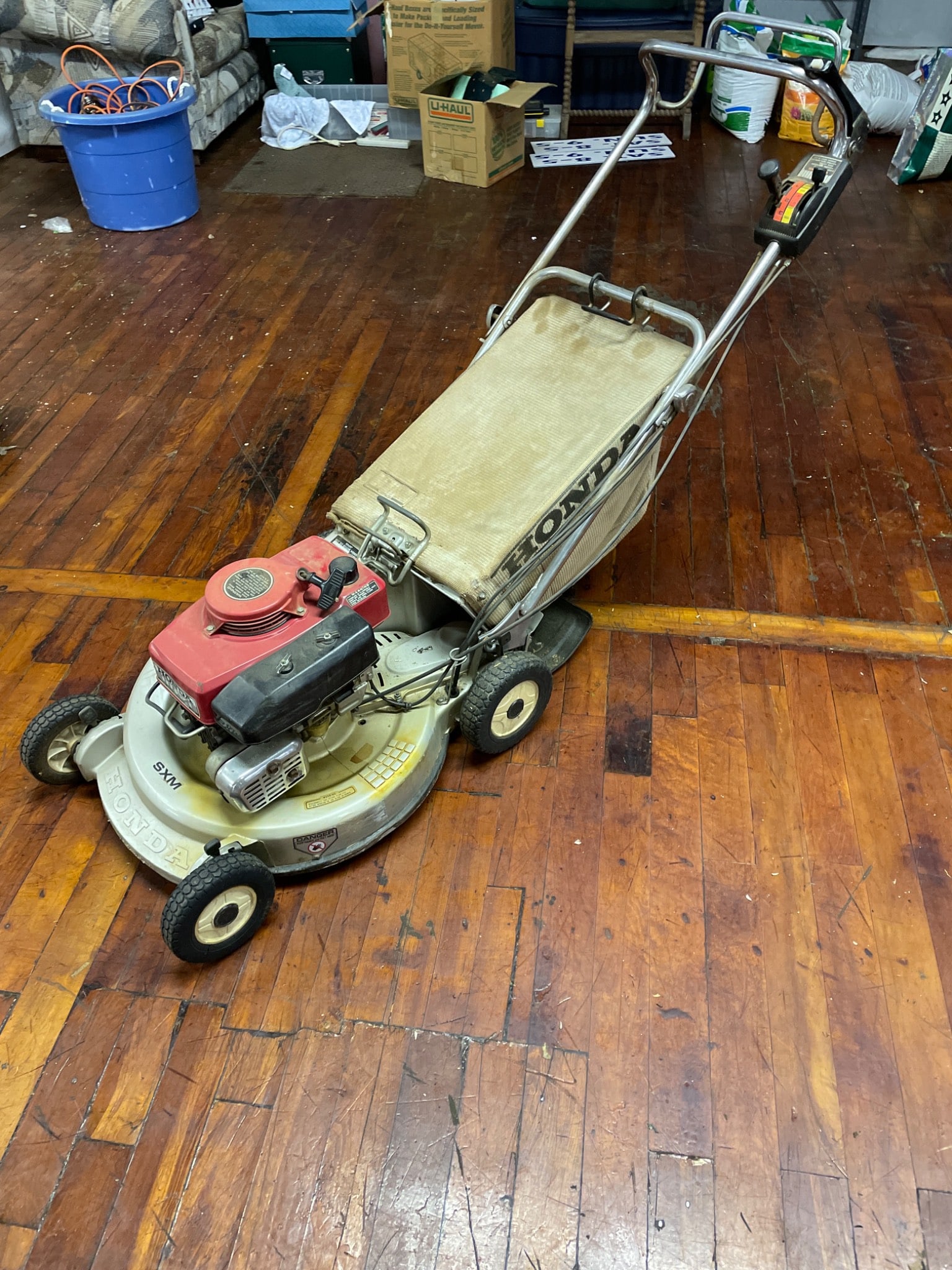 Honda SXM Gas-Powered Self-Propelled Lawn Mower With Collection Bag: This Honda SXM lawn mower features a gas-powered engine with a self-propelled system. The item cranks, runs, and the self-propulsion system operates as intended. It includes a built-in grass collectio