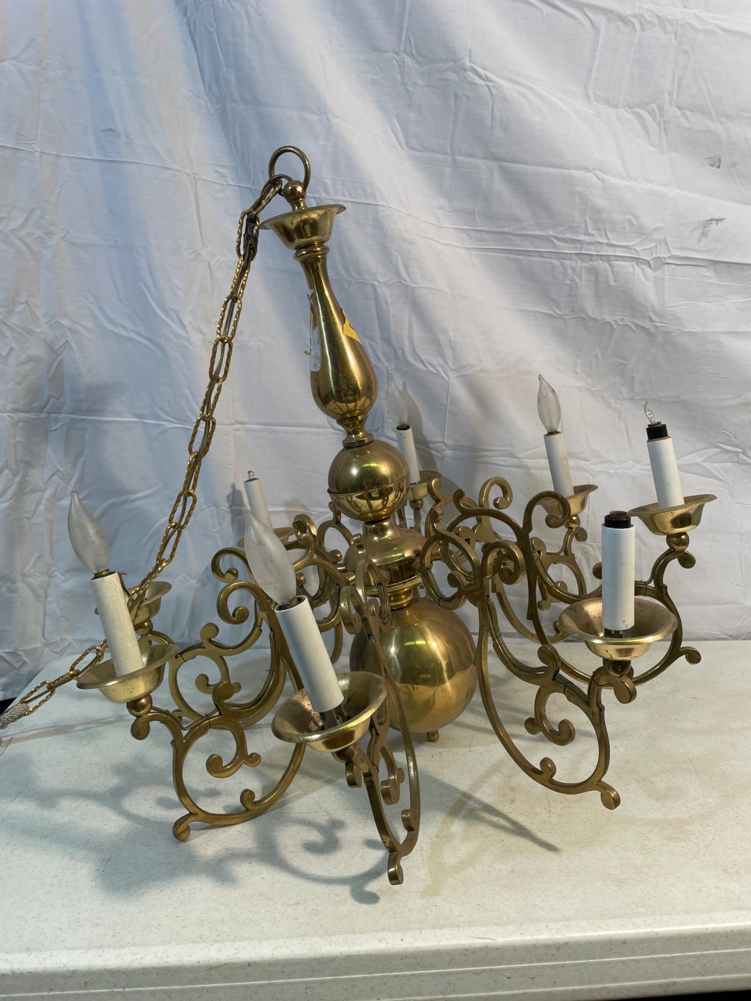 Brass 6-Arm Chandelier with Scrollwork Design and Chain Suspension: A brass chandelier featuring six arms adorned with intricate scrollwork, designed to hold candle-style bulbs. Includes an attached chain for suspension. Overall construction is brass with visible