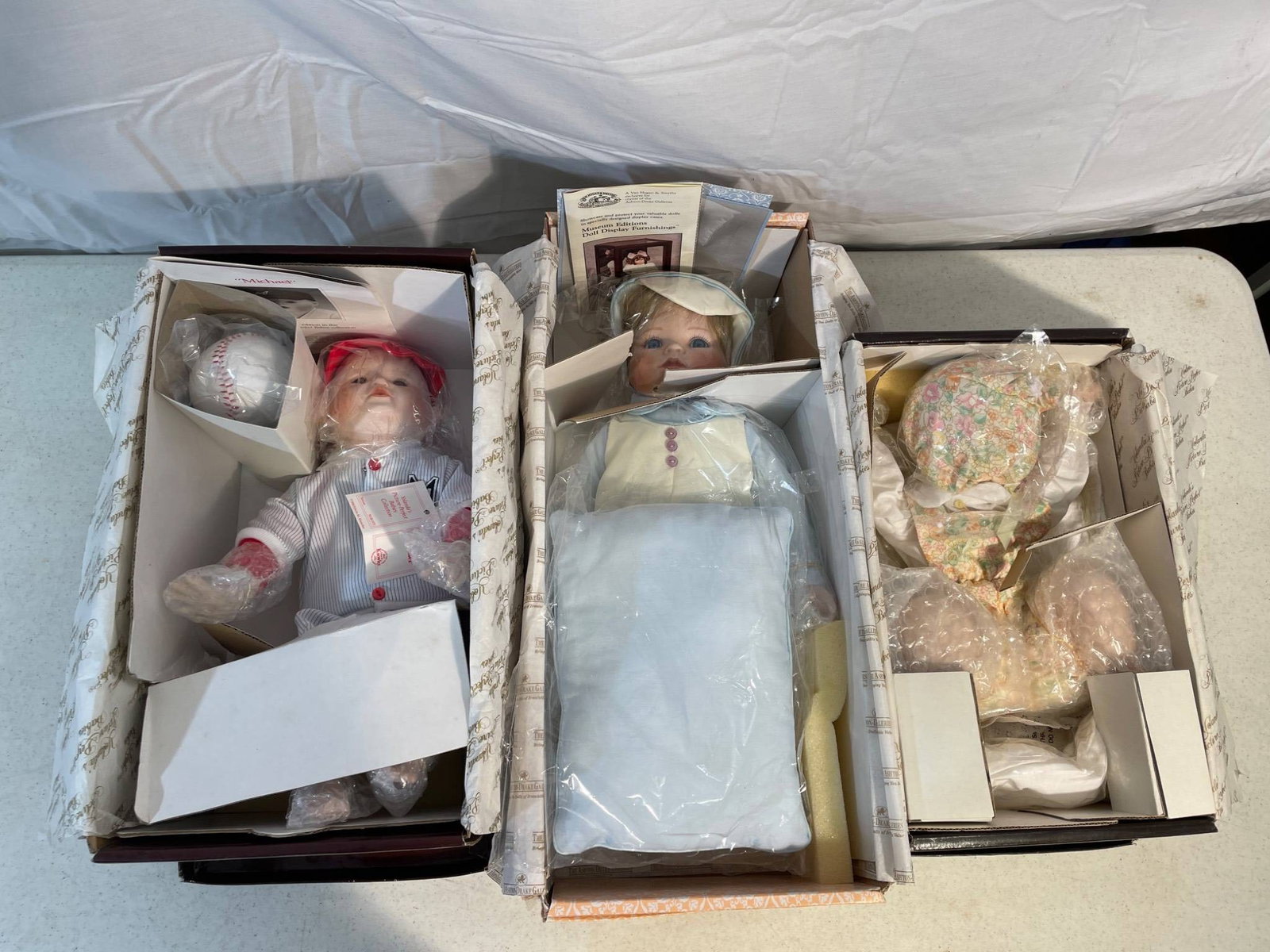 New Old Stock Porcelain Dolls in Original Packaging: This lot consists of multiple new old stock porcelain dolls, each housed in its original packaging. Includes dolls from notable brands such as The Ashton-Drake Galleries. Details and certifications ar