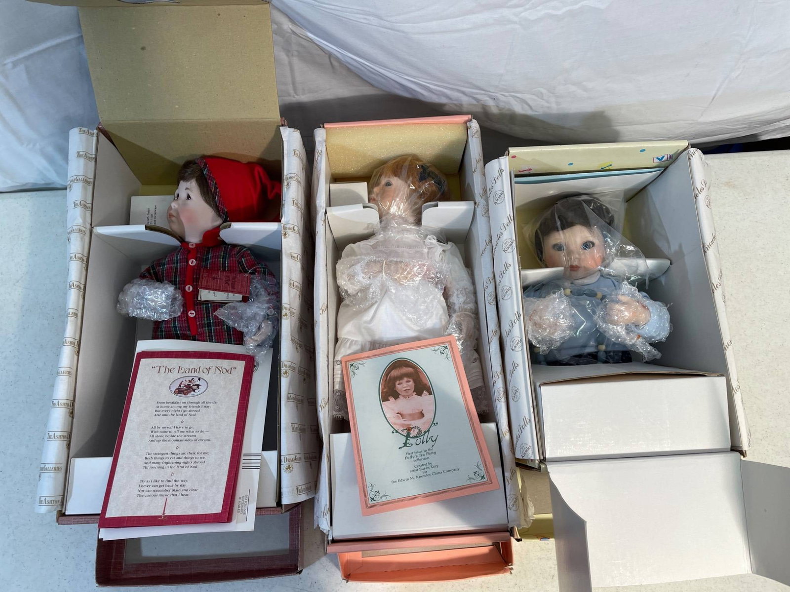 New Old Stock Porcelain Dolls With Original Boxes and Documentation: This lot includes three new old stock porcelain dolls, each presented in its original box, with accompanying documentation/booklets. Each doll is carefully wrapped and remains in unused condition.