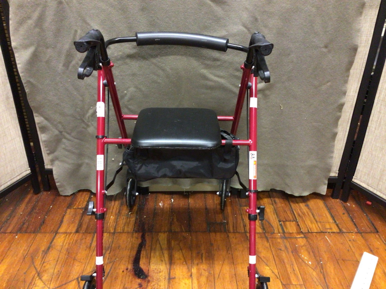 Red Four-Wheel Rolling Walker With Seat and Storage Bag: Four-wheel rolling walker with a red metal frame, padded seat, and under-seat storage bag. Features ergonomic handles with braking mechanisms. Includes adjustable height settings for user convenience.