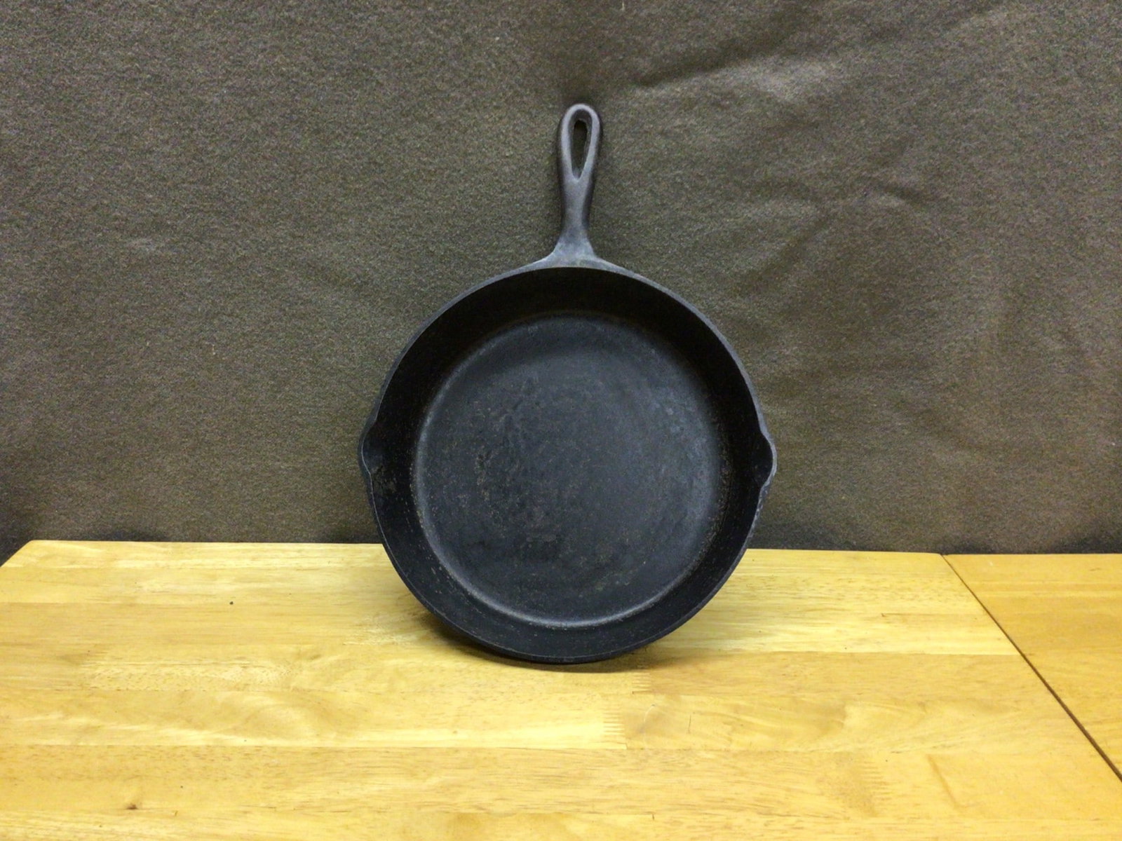 Cast Iron Skillet with Pour Spouts and Handle, Approx. 10 Inches Diameter: This is a cast iron skillet with an approximate 10-inch diameter, featuring two pour spouts on opposite sides and a single-loop handle. The skillet is shown to have a blackened patina consistent with