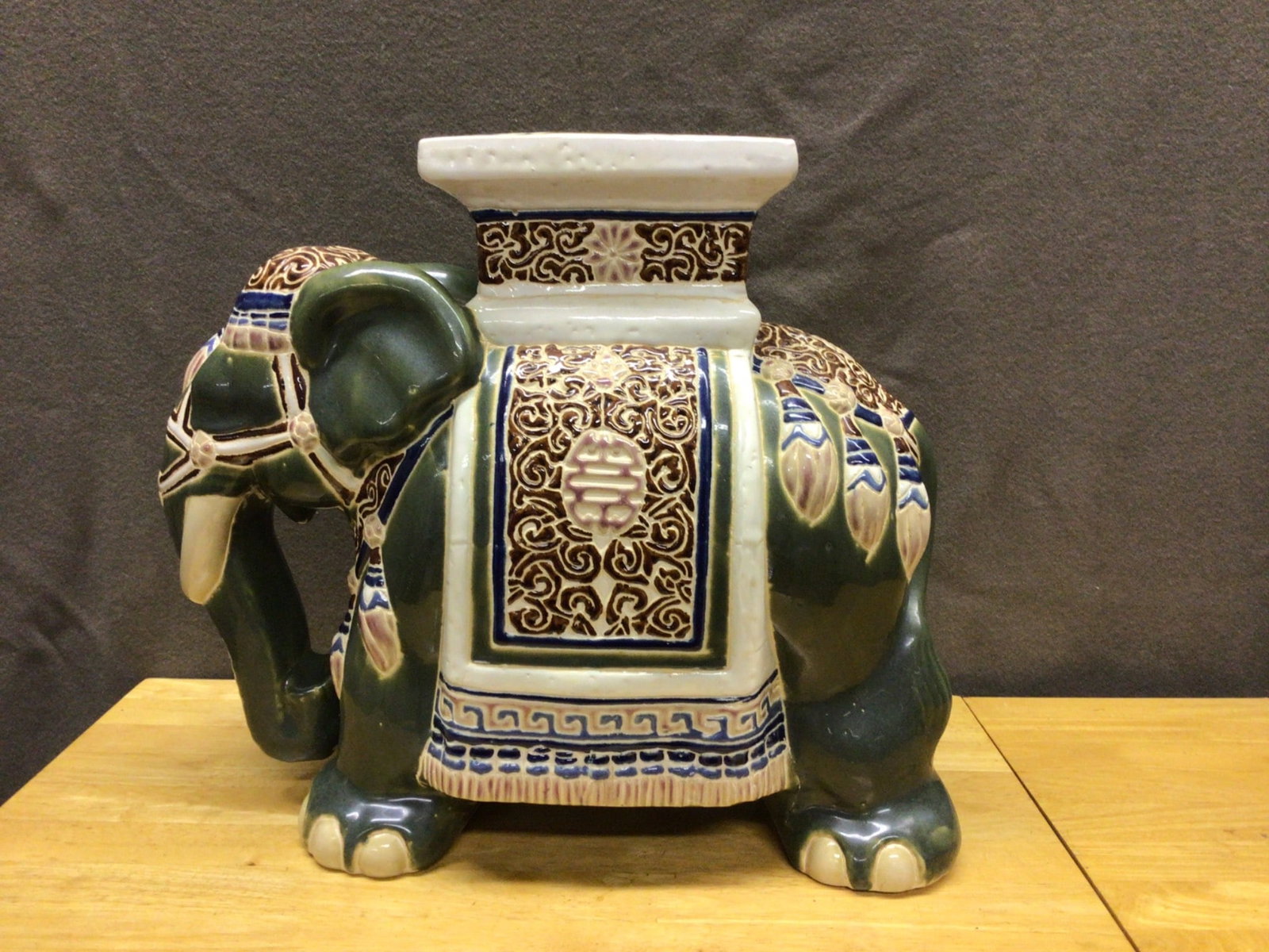 Ceramic Elephant Plant Stand with Decorative Glaze: This is a ceramic plant stand shaped like an elephant, featuring multicolored decorative glaze. The item has a rectangular platform on top and ornate patterns on the body. The dimensions, year of manu