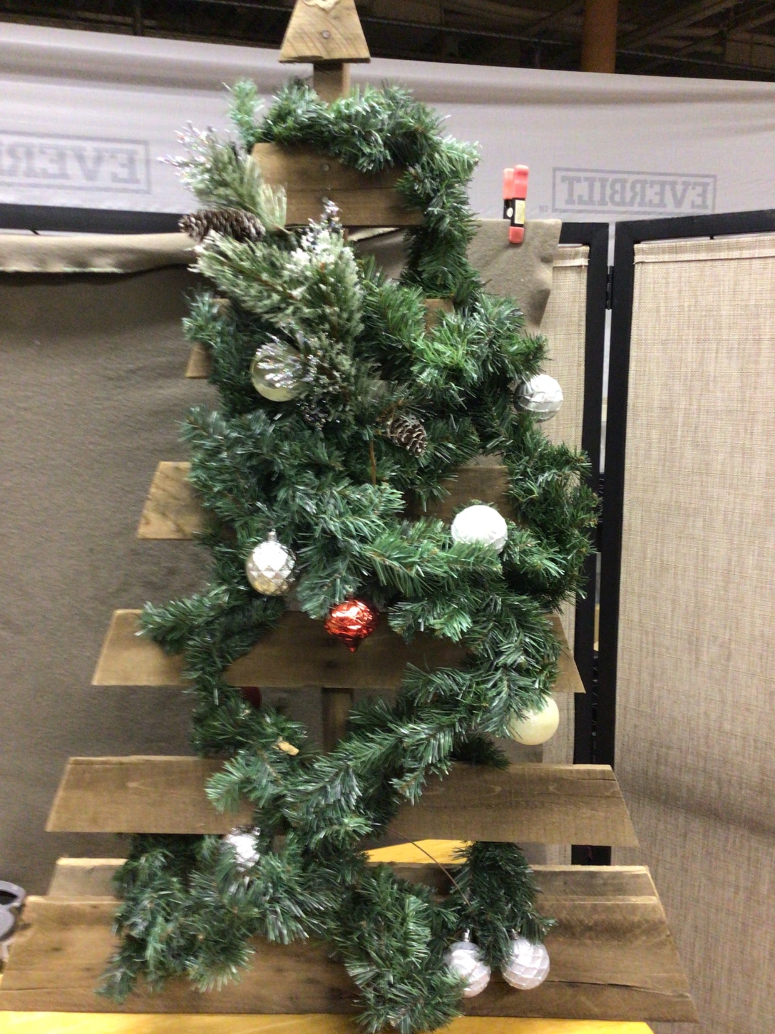 Wooden Christmas Tree With Faux Greenery and Decorative Ornaments: This lot includes a handcrafted wooden Christmas tree structure with faux greenery and various ornaments. The tree is adorned with garlands and a mix of decorative globes, pinecones, and accent