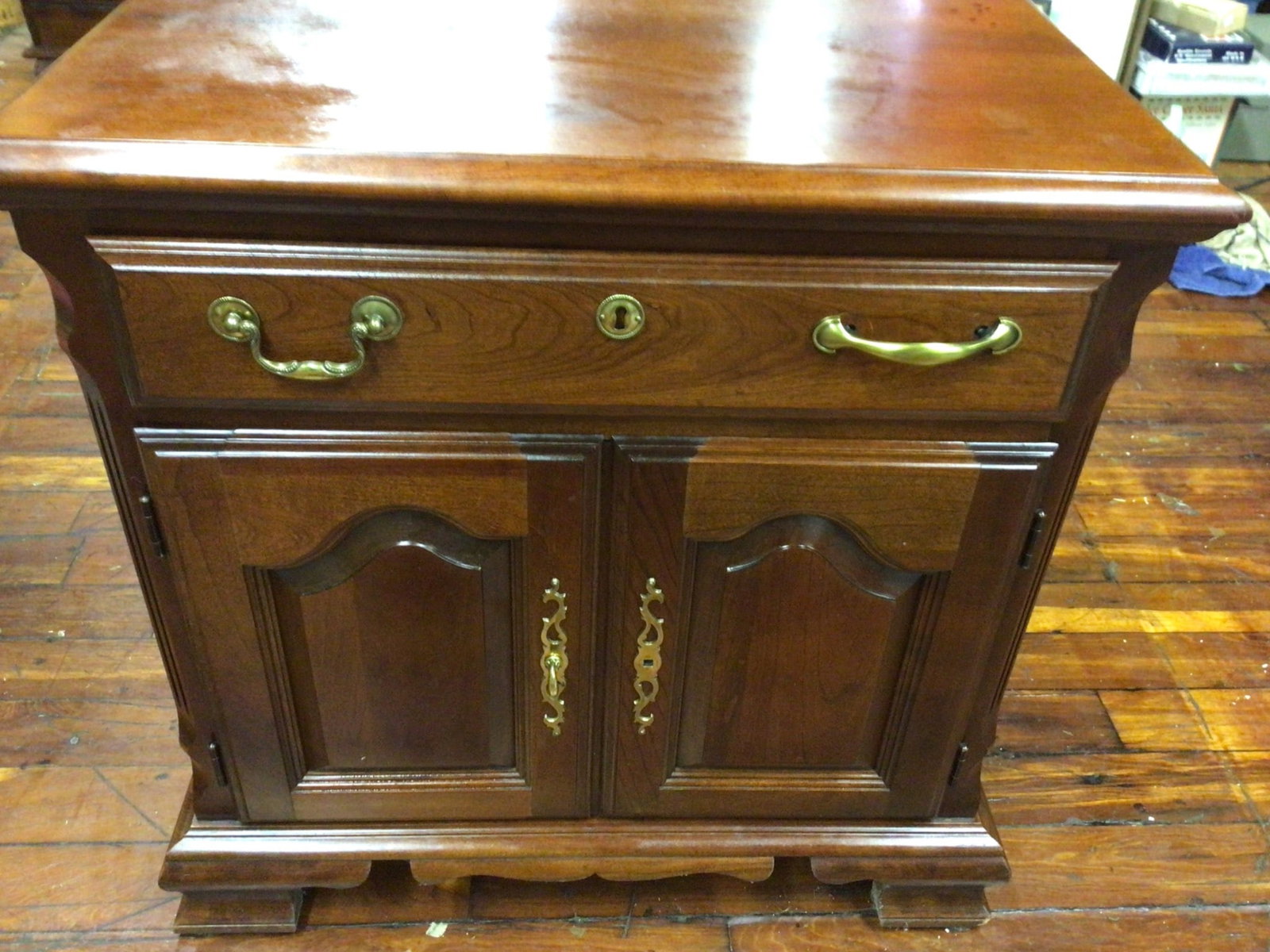 Wooden Sideboard With Drawer and Double Doors: This is a wooden sideboard featuring a single drawer with brass handles and a central keyhole. The unit also includes double doors below the drawer with brass hardware. Measuring approximately 22 inch