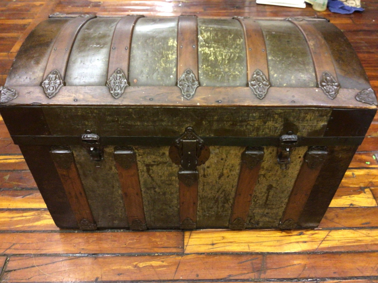 Wooden and Metal Steamer Trunk with Domed Lid and Decorative Hardware: Domed-top steamer trunk constructed with wood panels and metal accents. Features decorative metal hardware, hinges, and sturdy latches for closure. Interior lined with patterned paper, bearing wear an