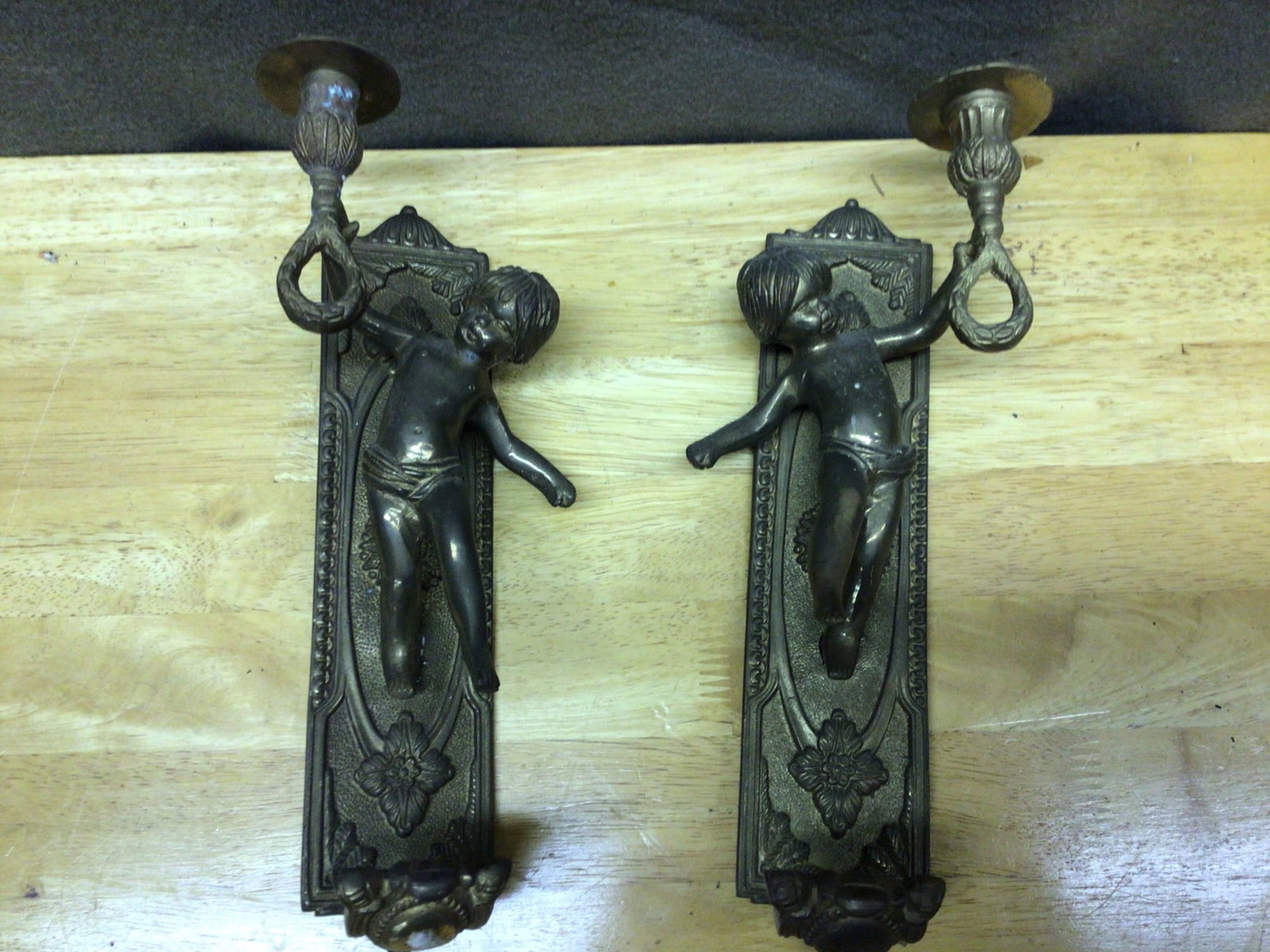 Wall-Mounted Candle Holders with Cherub Design, Made in India: This lot includes a pair of brass or bronze wall-mounted candle holders featuring cherub designs. The holders are designed with intricate detailing and include mounting holes on the back for secure at