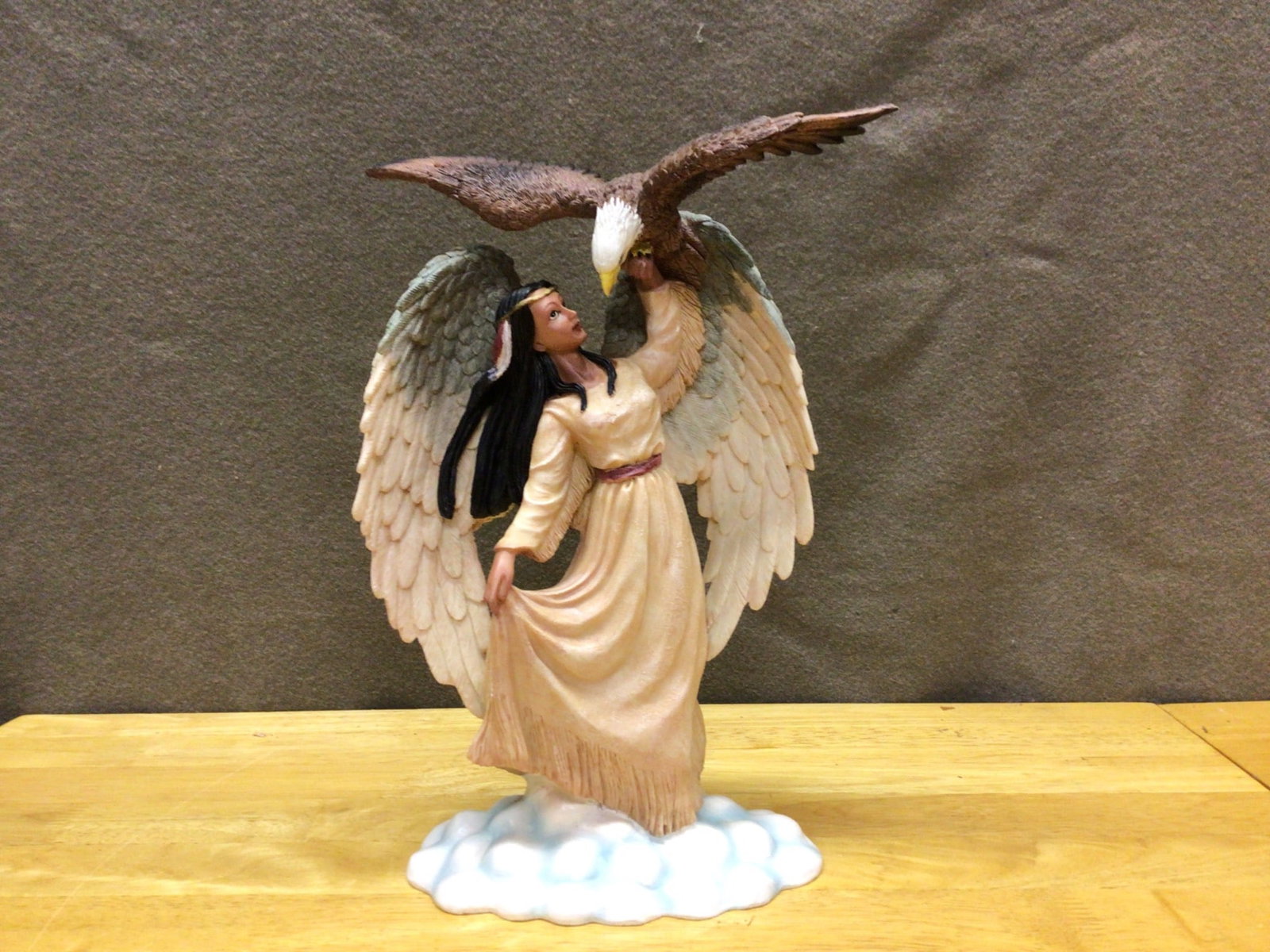 Figurine Depicting Angelic Woman with Eagle on Cloud Base: Polyresin figurine featuring a woman with angel wings and a bald eagle perched on her raised hand, set on a cloud-shaped base. Approximate height is 12 inches, as shown next to a ruler. Detailing