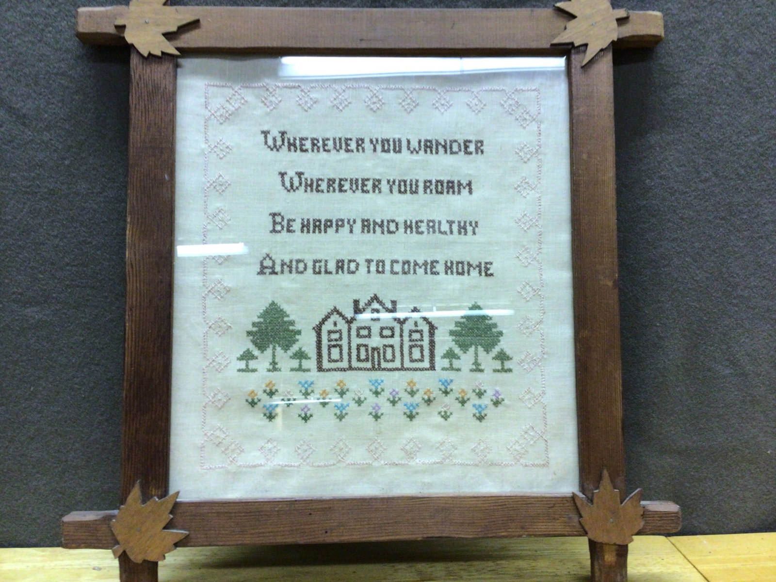 Hand-Stitched Cross-Stitch Framed Artwork with Wooden Frame: This is a hand-stitched cross-stitch artwork featuring an inspirational quote and house design, framed in decorative wood with leaf-shaped accents at corners. The frame is assembled with a back paper 