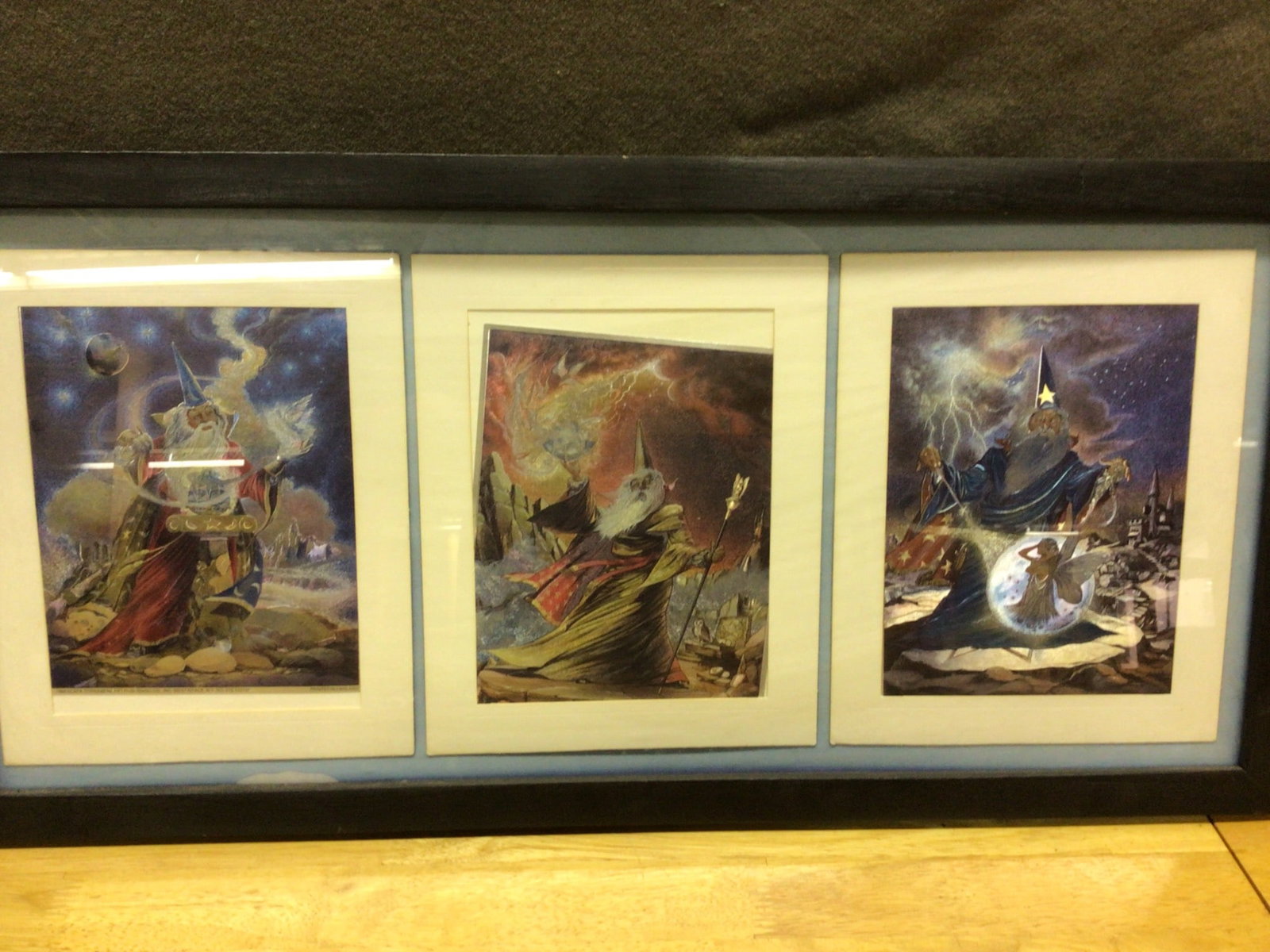 Framed Triptych Print Series Featuring Wizard and Fantasy Imagery: A framed triptych of prints featuring a wizard and fantasy-scape scenes. Each print depicts a wizard in a different setting, including cosmic and magical landscapes. The series is framed under glass