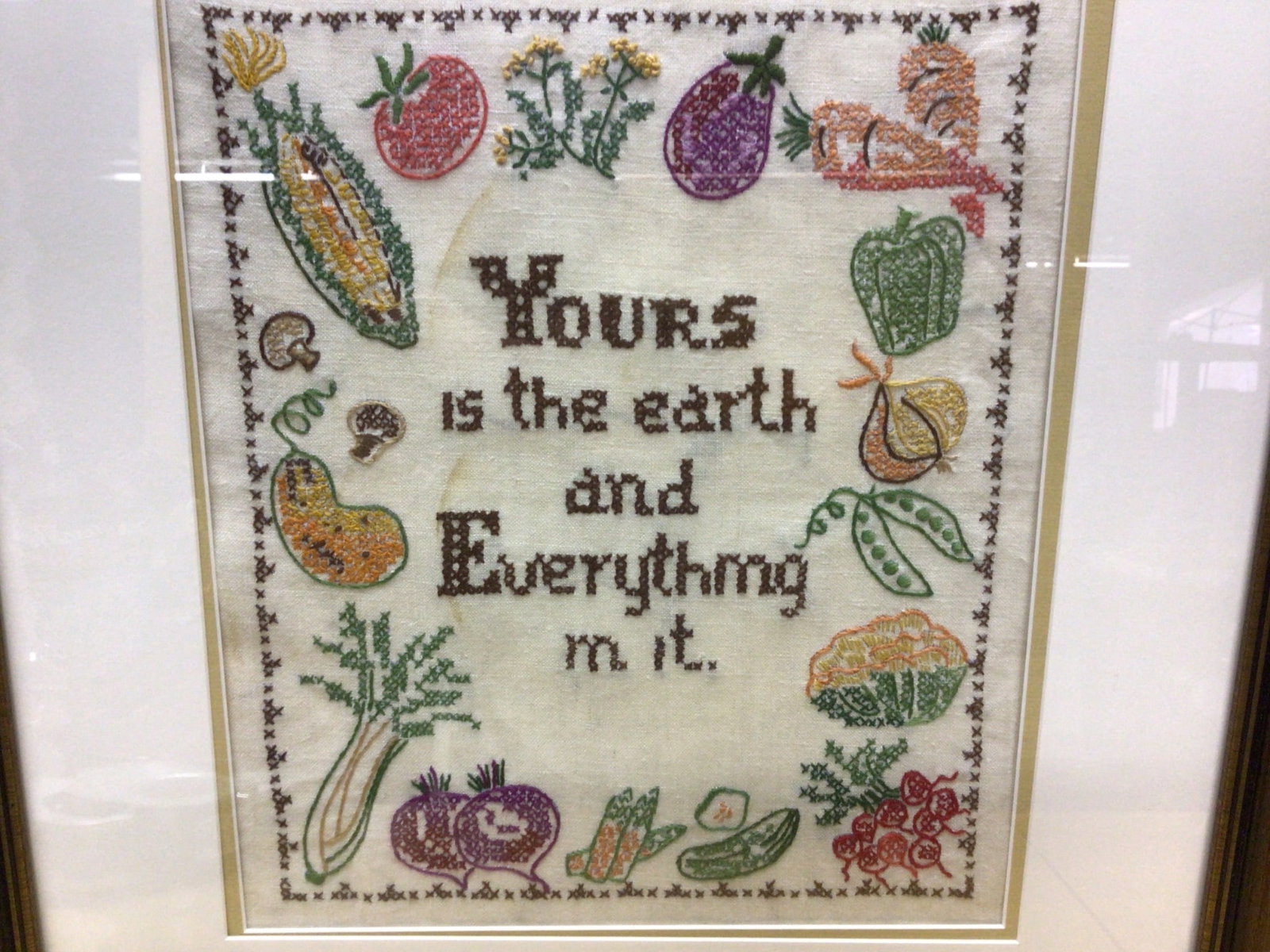 Hand-Stitched Framed Embroidery Featuring Fruits and Vegetables: This is a hand-stitched embroidery piece showcasing an assortment of fruits and vegetables surrounding the text, 'Yours is the earth and everything in it.' The item features a decorative border, is