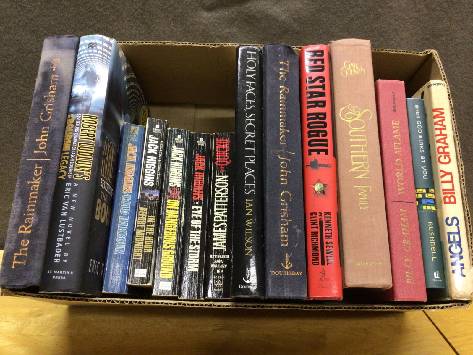 Hardcover and Paperback Books by Various Authors: This lot includes a selection of hardcover and paperback books by authors like John Grisham, Robert Ludlum, Jack Higgins, Kenneth Sewell, and others. Titles include 'The Rainmaker,' 'The Bourne Legacy