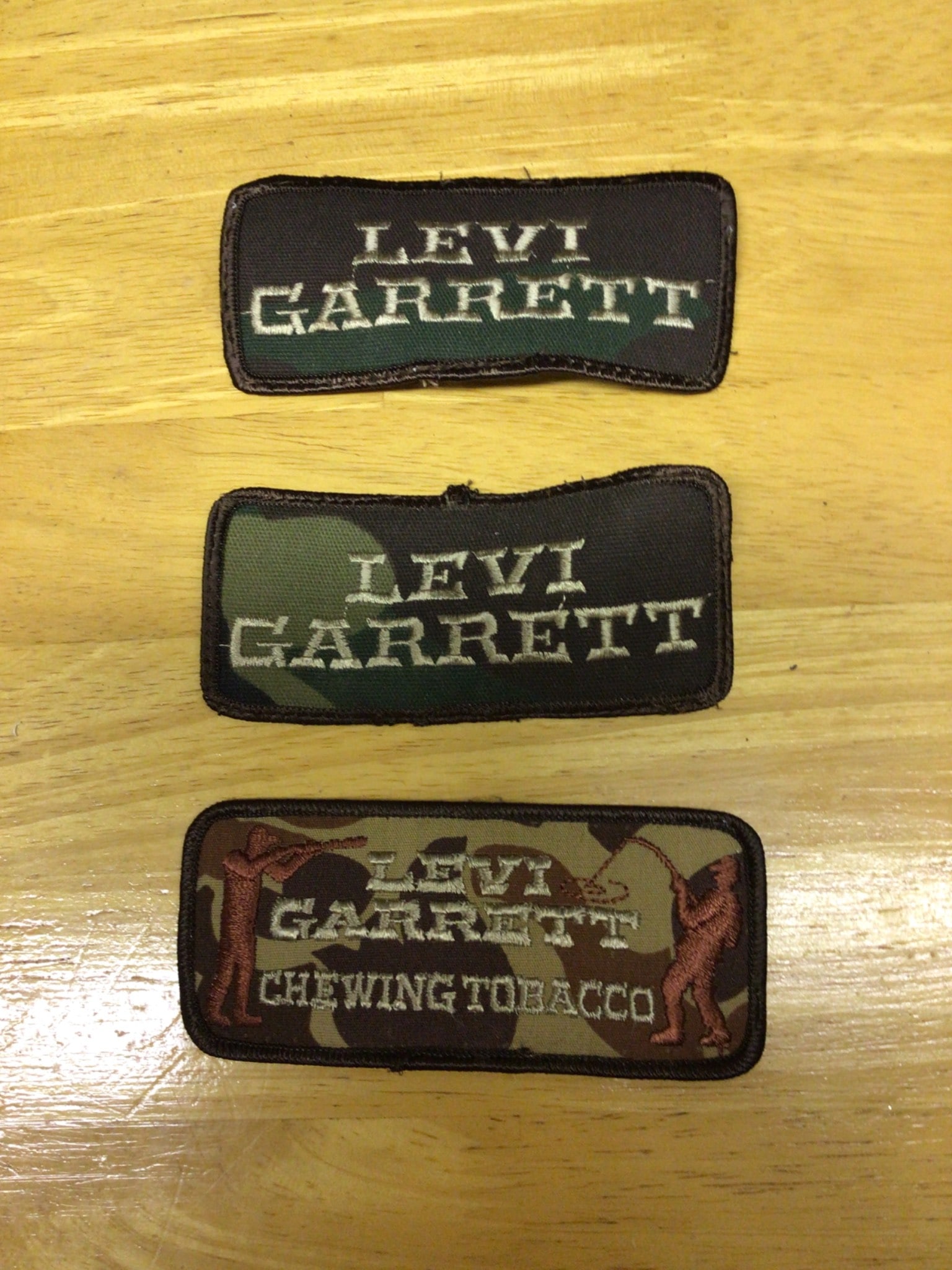 Levi Garrett Chewing Tobacco Patches in Various Designs: This lot consists of three Levi Garrett patches featuring the brand logo. The designs include two camouflage patterns and one brown solid pattern with the text 'Levi Garrett Chewing Tobacco.' Each pat