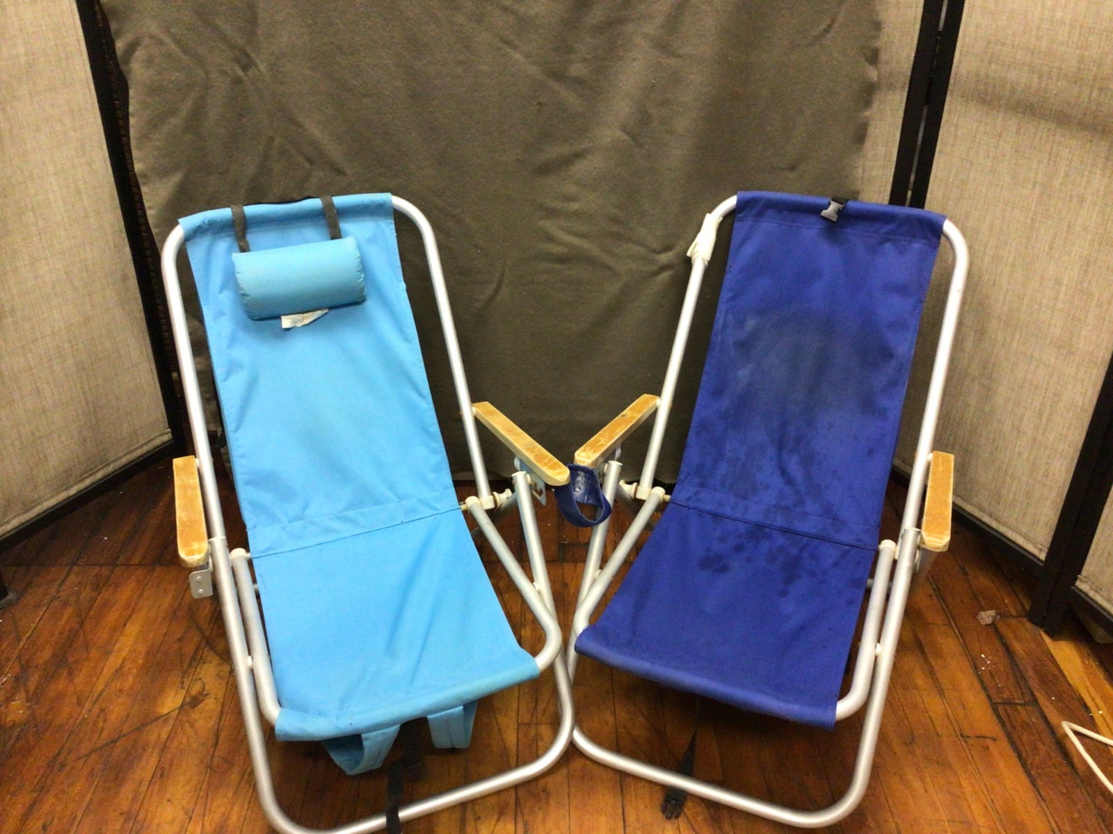 Two Folding Aluminum Frame Beach Chairs With Nylon Fabric: Two folding beach chairs with aluminum frames and nylon fabric seats. The set includes one blue and one light blue chair. Both chairs feature wooden armrests and an adjustable headrest on the light bl